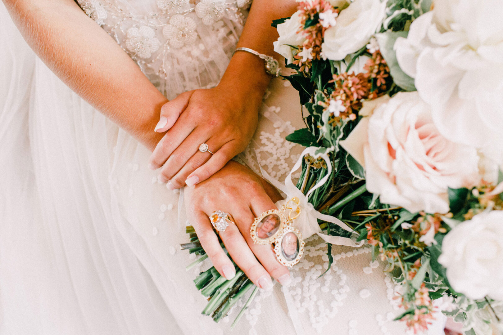 Close-up of a bride's hands holding a bouquet of flowers at her Willow Creek Winery wedding. She wears a wedding dress, an engagement ring, and ornate rings.