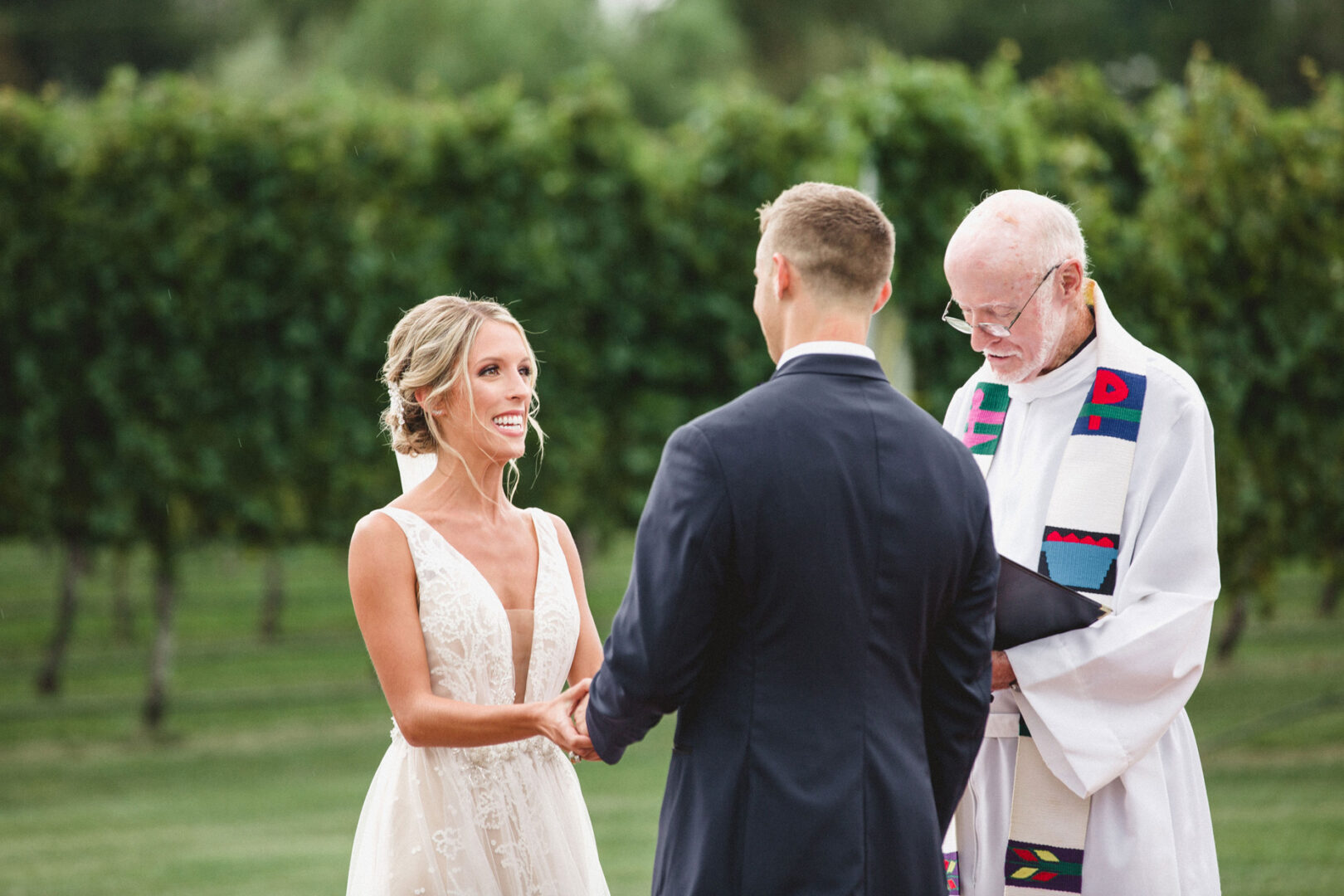 A couple holding hands during their Willow Creek Winery wedding, with an officiant in a white robe standing beside them in the beautiful outdoor setting.
