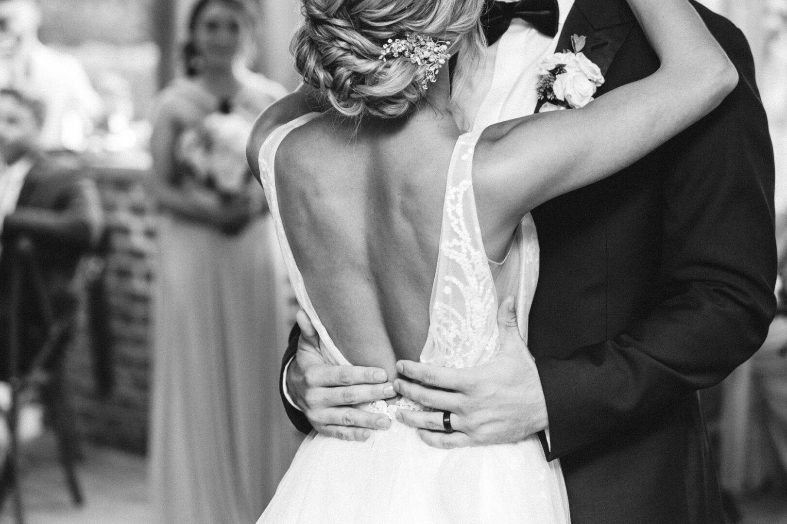 At a picturesque Willow Creek Winery wedding, a couple in formal attire shares a dance. The woman is wearing a dress with an open back, while the man is elegantly dressed in a suit and bow tie, under the vineyard's charming lights.