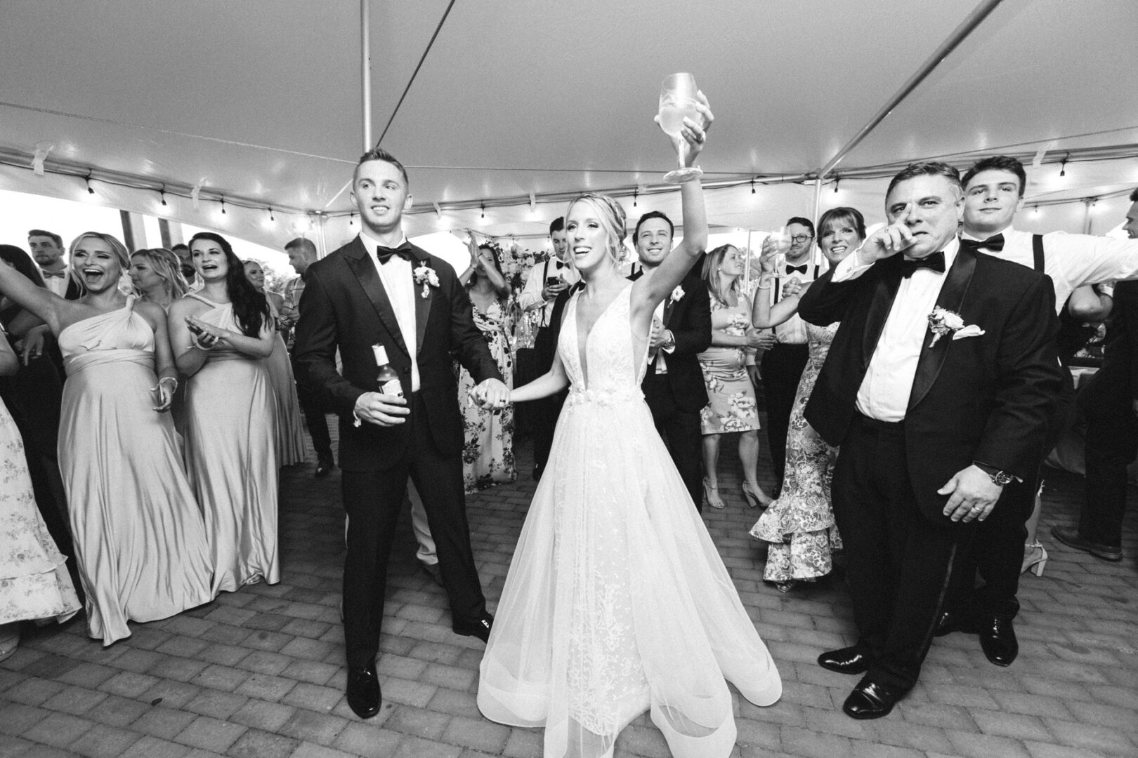 At the Willow Creek Winery wedding, the bride and groom celebrate with guests under a tent. The bride raises her glass, and everyone appears joyful.