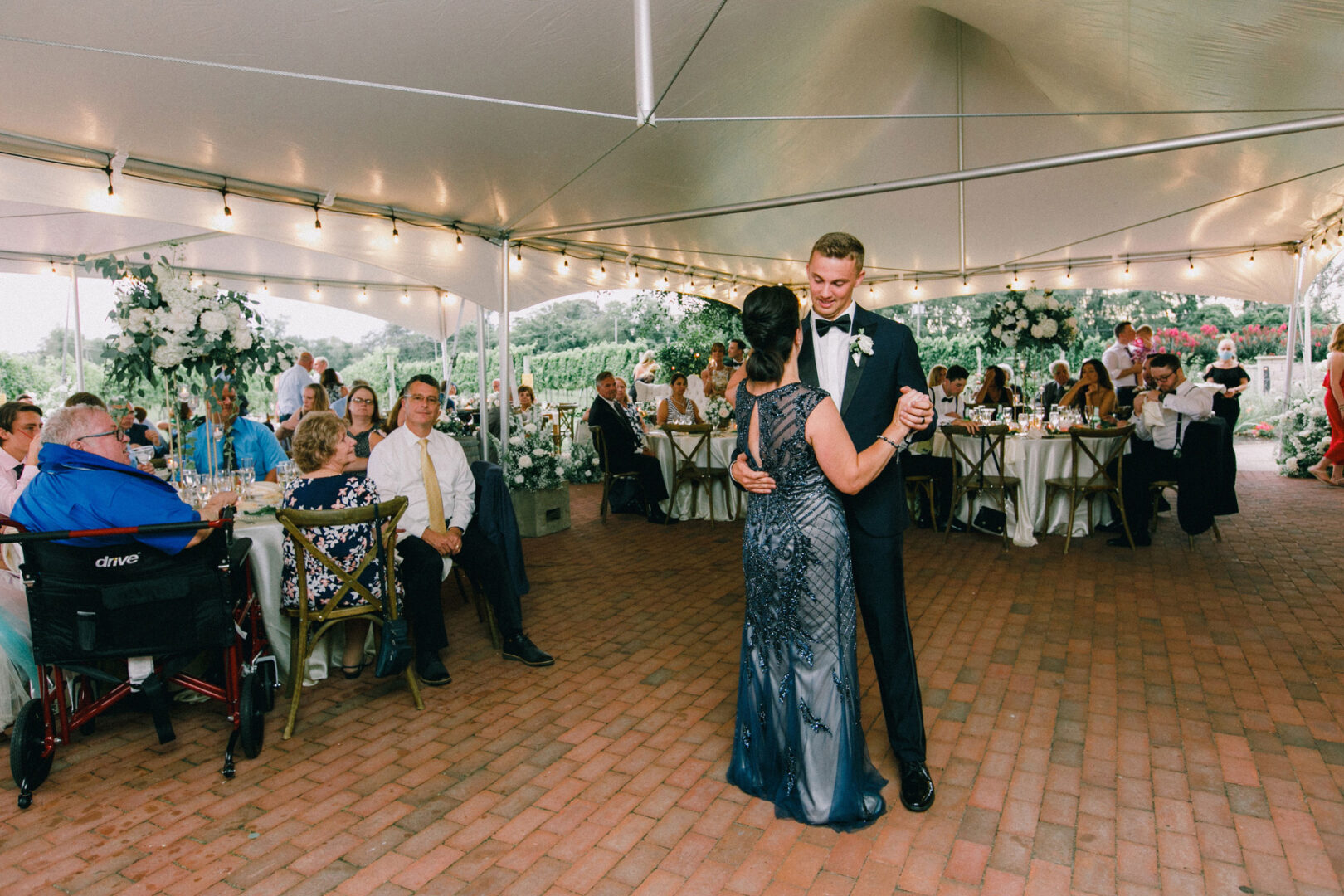 At a charming Willow Creek Winery wedding, a man and a woman dance gracefully under the tent as guests seated at tables look on with delight.