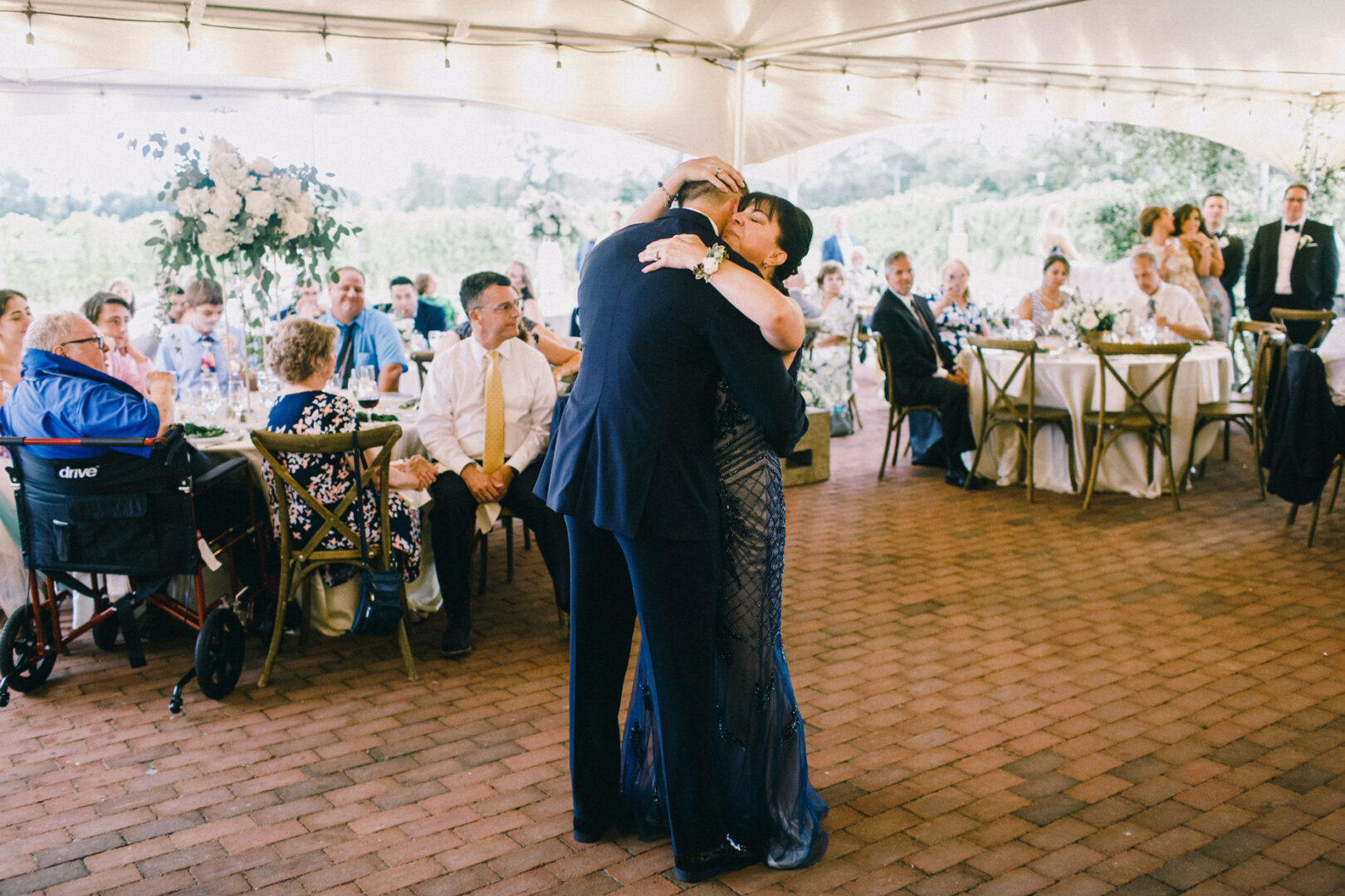 At a Willow Creek Winery wedding, a couple dances embraced at a formal outdoor event, with seated guests watching on under the canopy.