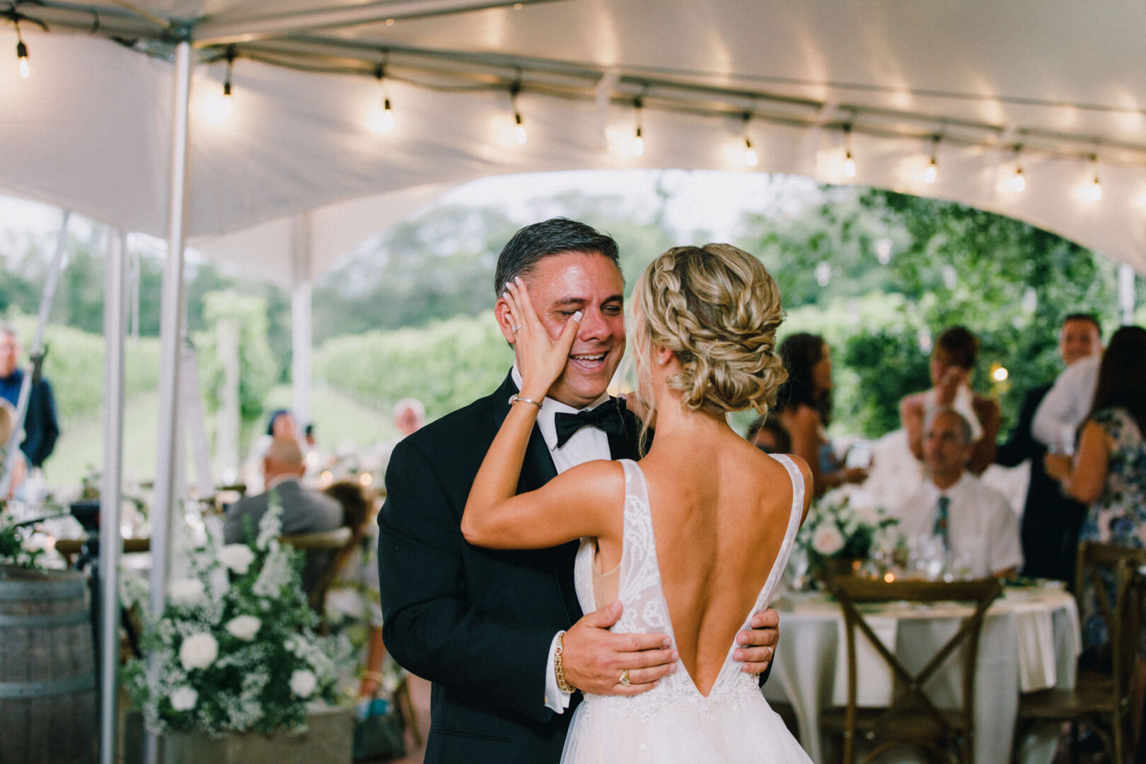 At a Willow Creek Winery wedding, a couple shares a dance under a canopy, surrounded by floral decorations, while guests enjoy the enchanting vineyard backdrop.