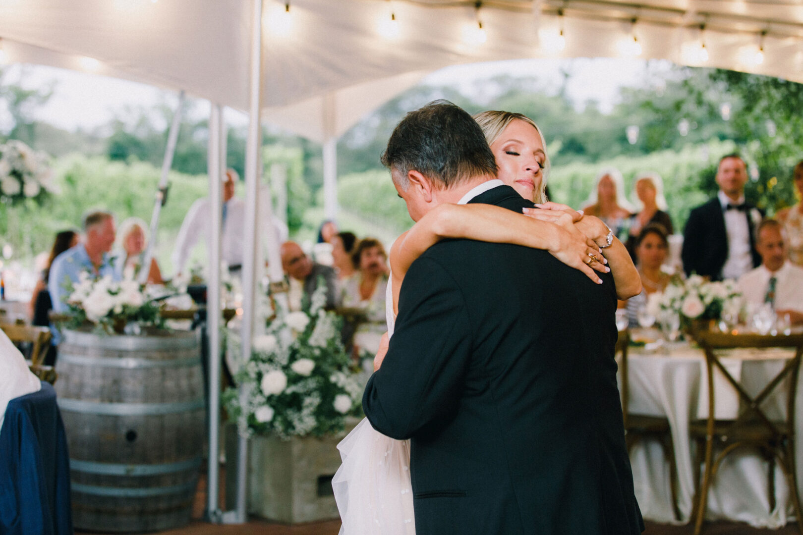 At a picturesque Willow Creek Winery wedding, a couple dances gracefully under a white tent, surrounded by elegantly set tables and delighted guests.