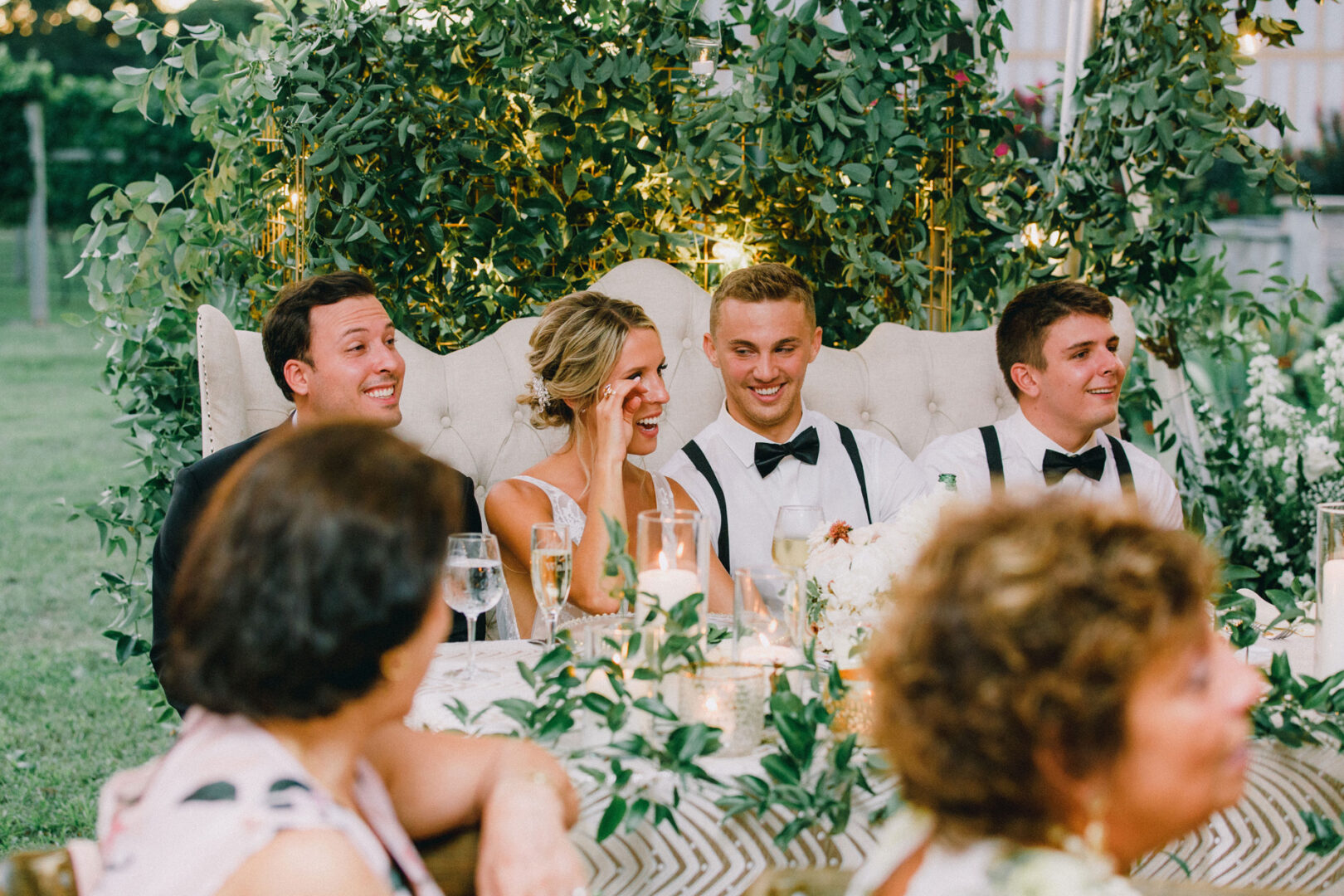 Four people sit at a beautifully decorated table during an outdoor event, surrounded by the lush greenery and vibrant flowers of Willow Creek Winery, creating an enchanting wedding atmosphere.