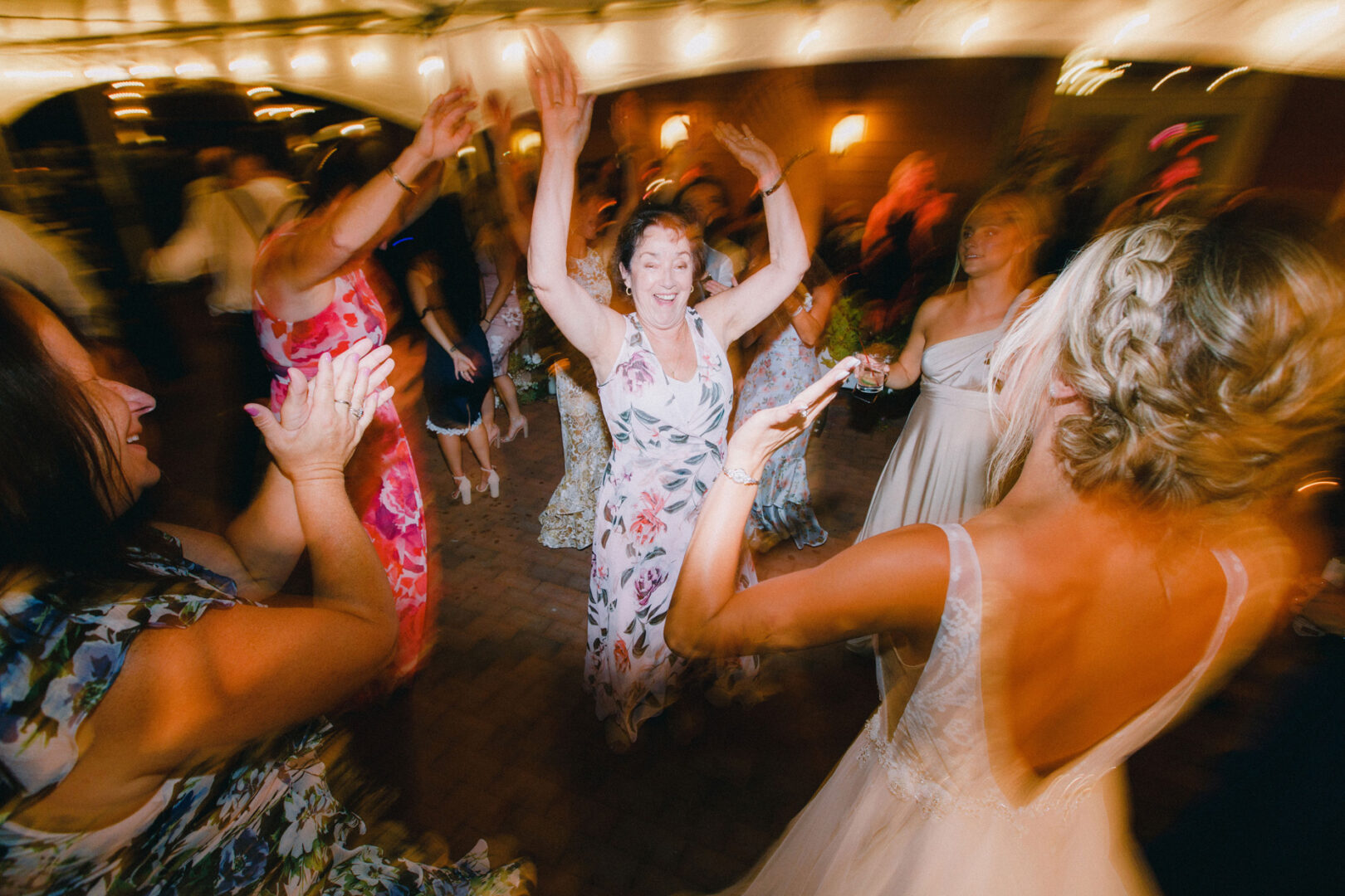 A lively group of people is dancing joyfully at the party, with blurred motion capturing their movements, as if celebrating a magical evening at a Willow Creek Winery wedding.