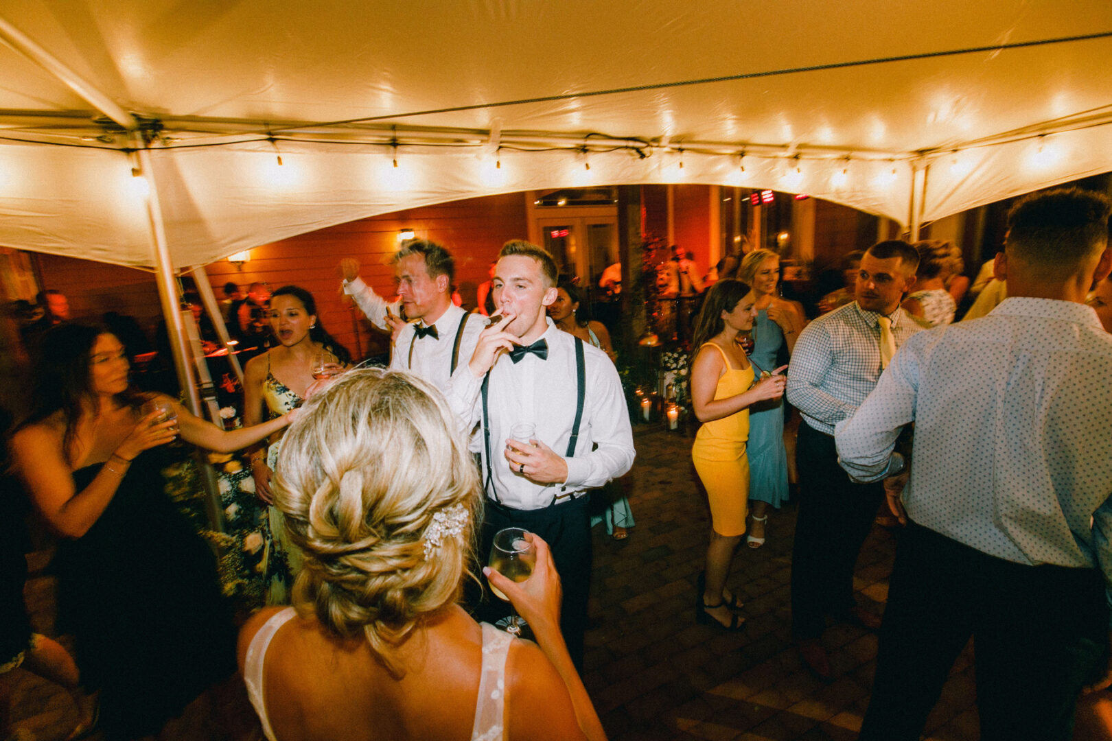 A group of people in formal attire dance and socialize under a tent with string lights at a night event, celebrating a Willow Creek Winery wedding.