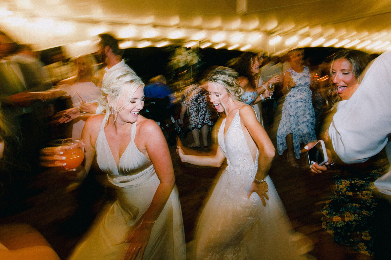 Amid the enchanting ambiance of Willow Creek Winery, guests, including a bride in a white gown, are dancing energetically under string lights at this lively indoor wedding event.