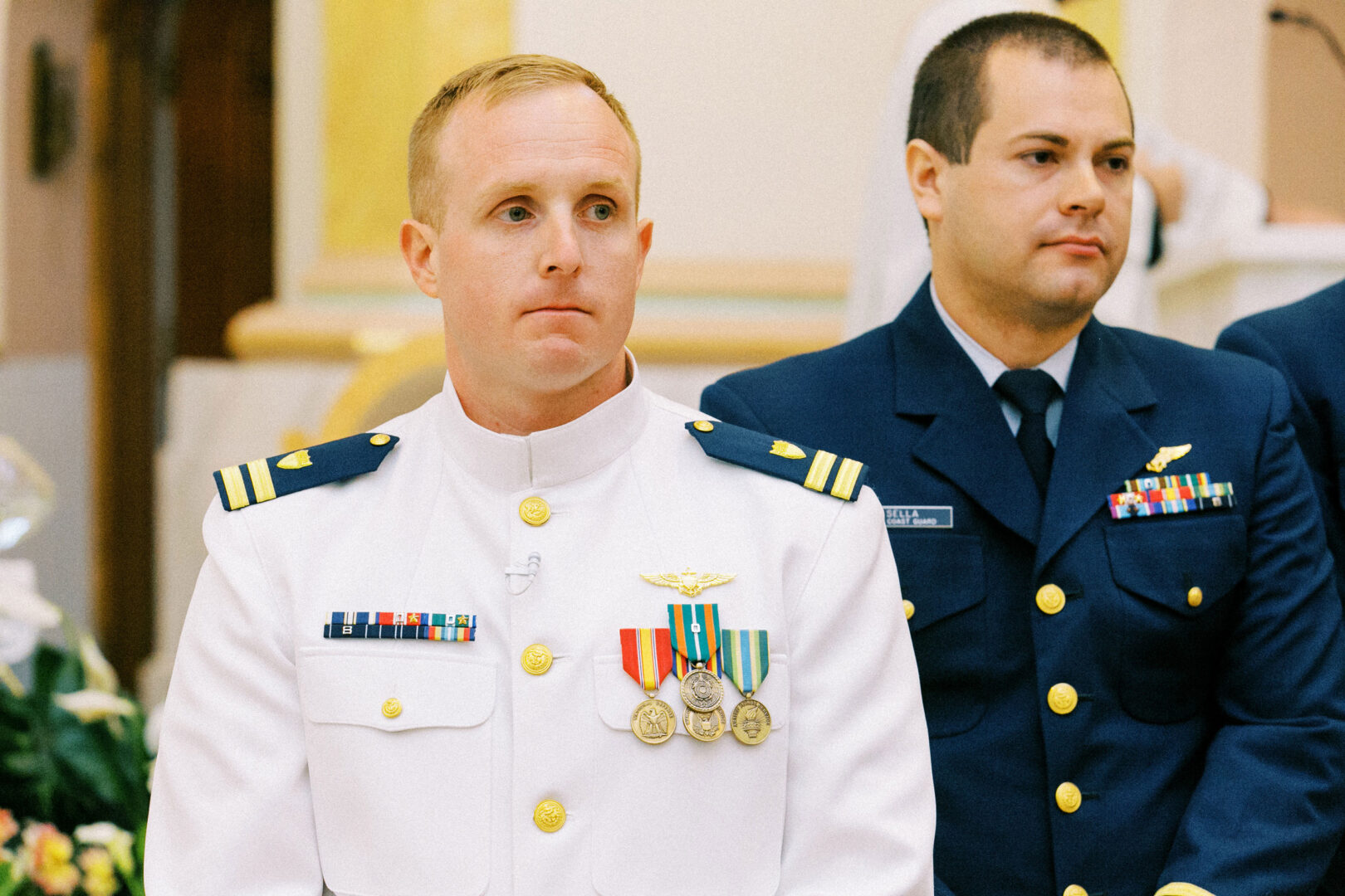 Two uniformed military personnel stand side by side at a wedding by the beach in Cape May, one in a white uniform adorned with medals, the other in a blue uniform.