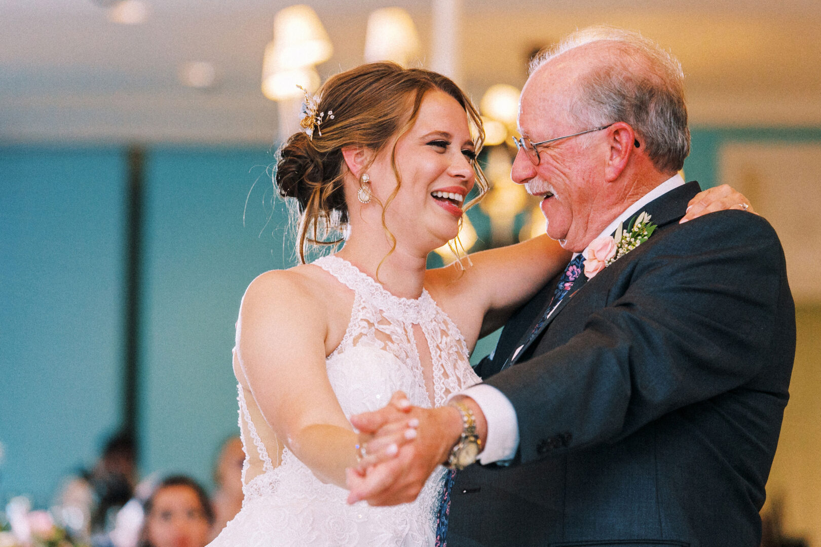 A bride and an older man, likely her father, smile and dance together in a warmly lit room at their wedding by the beach in Cape May.