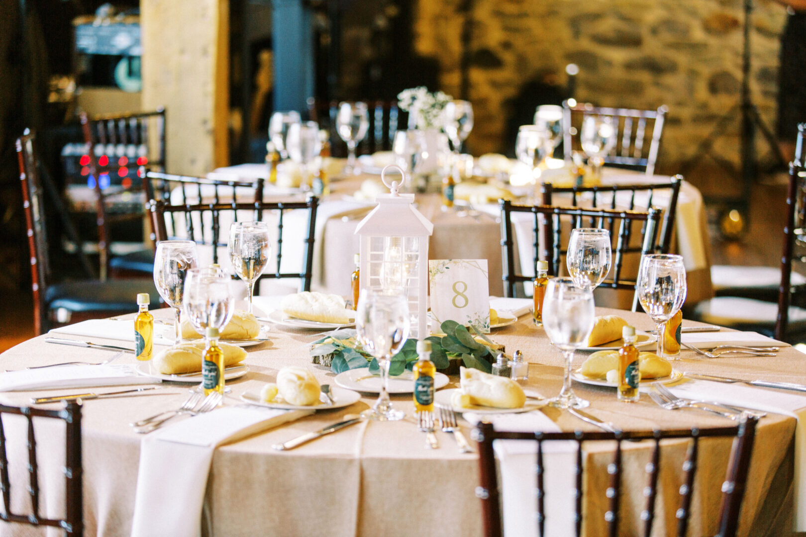 Elegant dining table set for an event at Harvest View Barn at Hershey Farms Wedding, featuring a white tablecloth, glassware, silverware, and a white lantern centerpiece with greenery and table number eight.