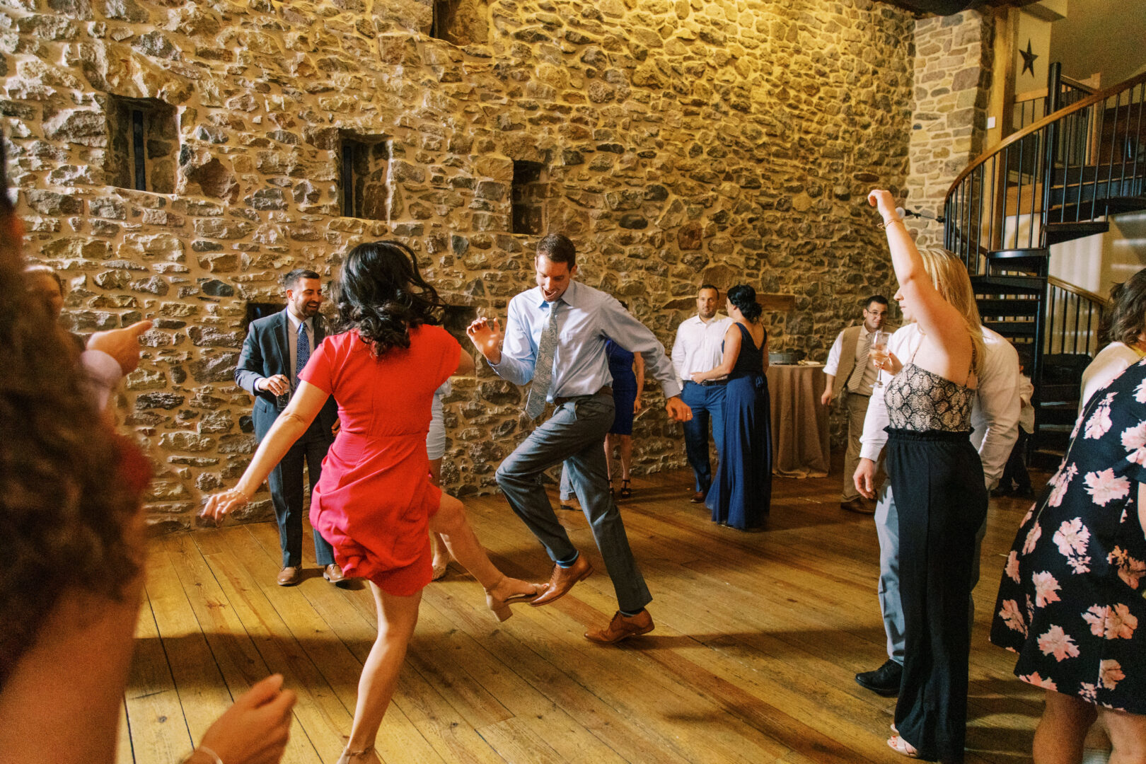 Dancers moved energetically on the wooden floor, their steps echoing off the stone walls and spiral staircase of Harvest View Barn at Hershey Farms, creating a lively atmosphere perfect for a wedding celebration.