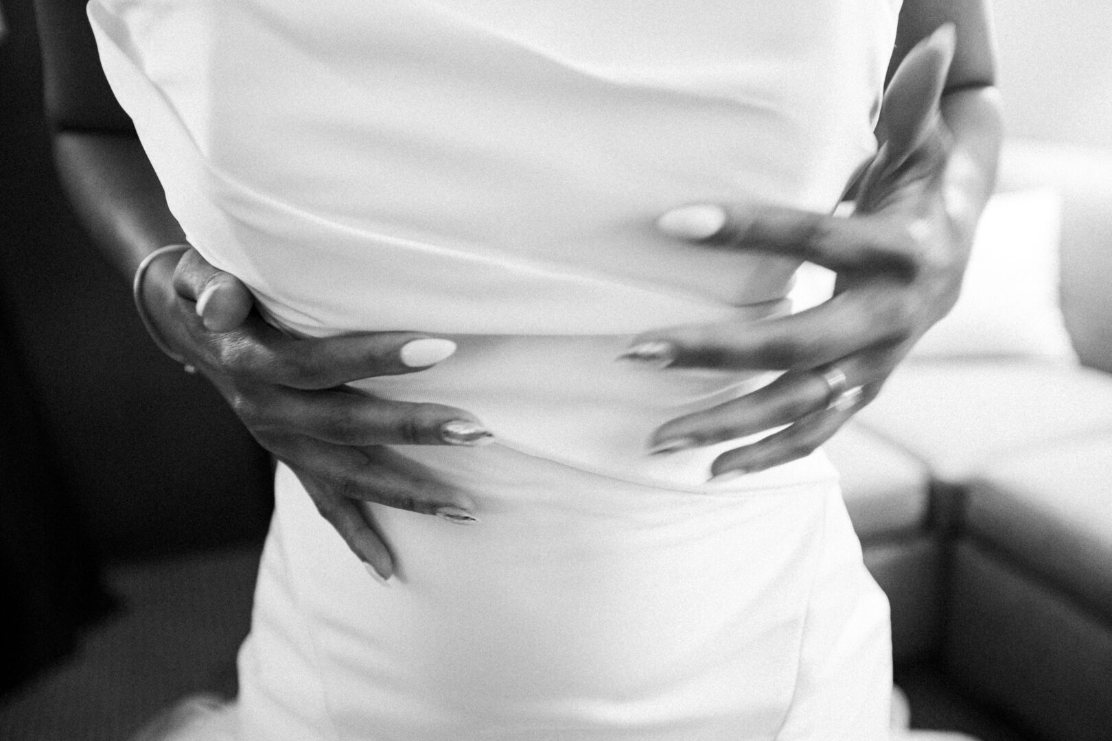 A close-up of hands hugging a person in a white dress, captured at a Mansion on Main Street Wedding. The focus rests on the embrace and the intricate texture of the dress in this black and white image.