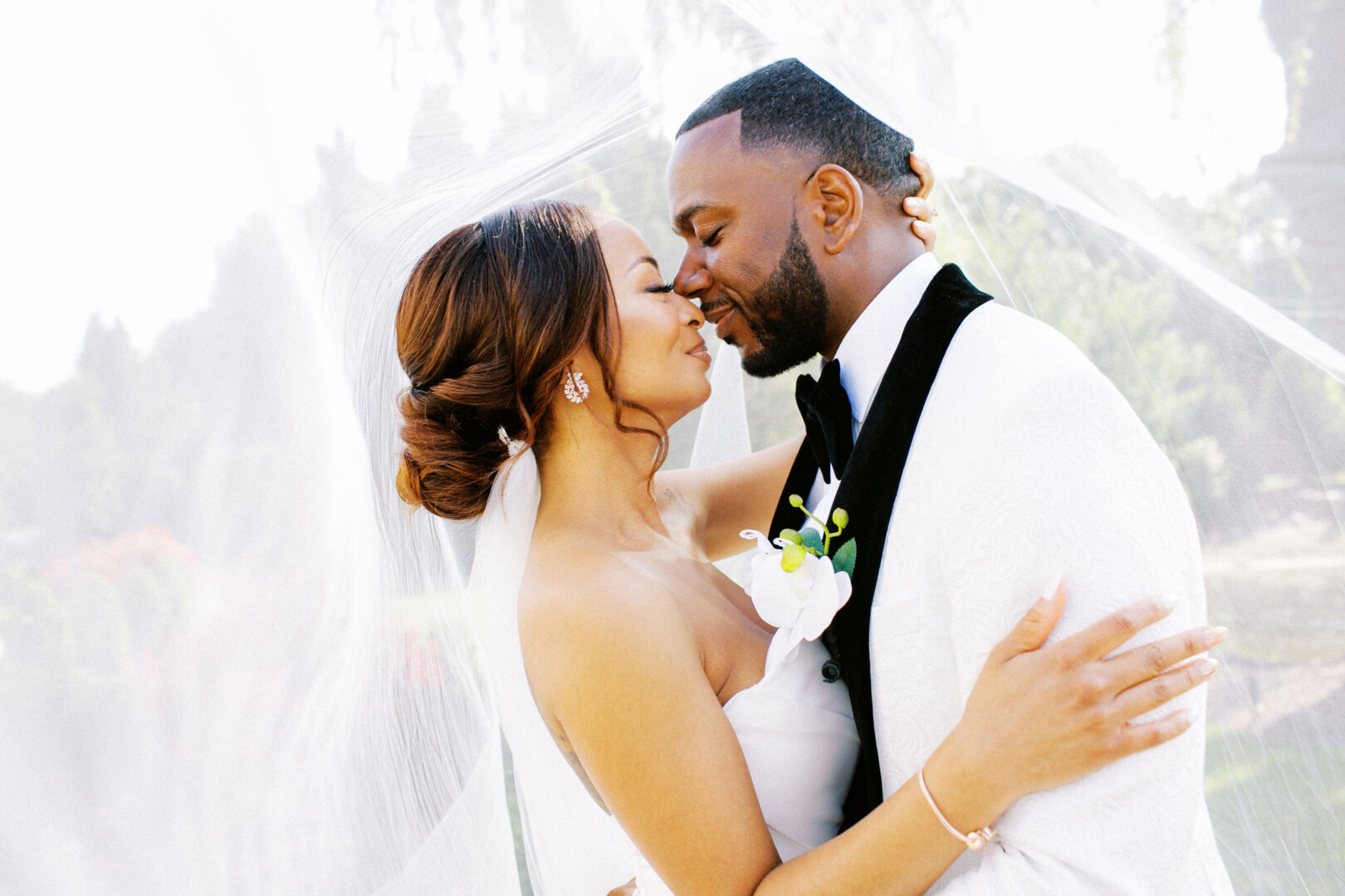 At their Mansion on Main Street wedding, the bride and groom share a tender moment under a veil in an enchanting outdoor setting.