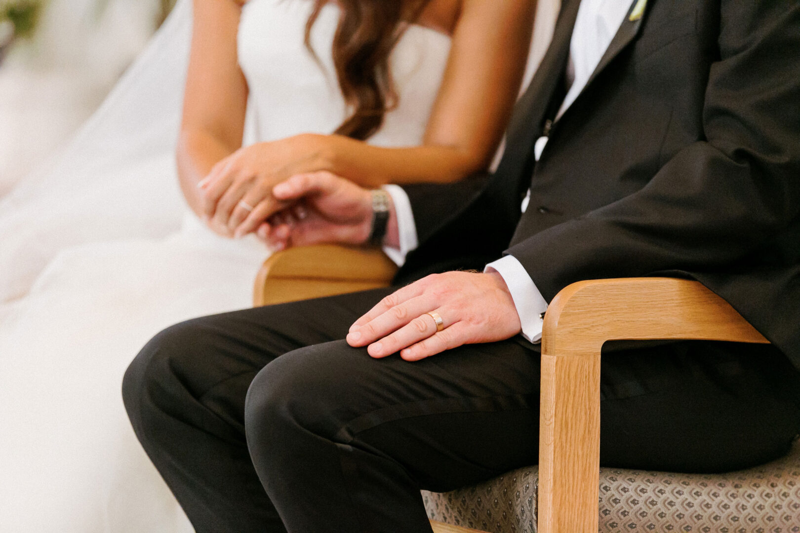 At a charming Willow Creek Winery wedding, the bride and groom sit together on wooden chairs, holding hands.