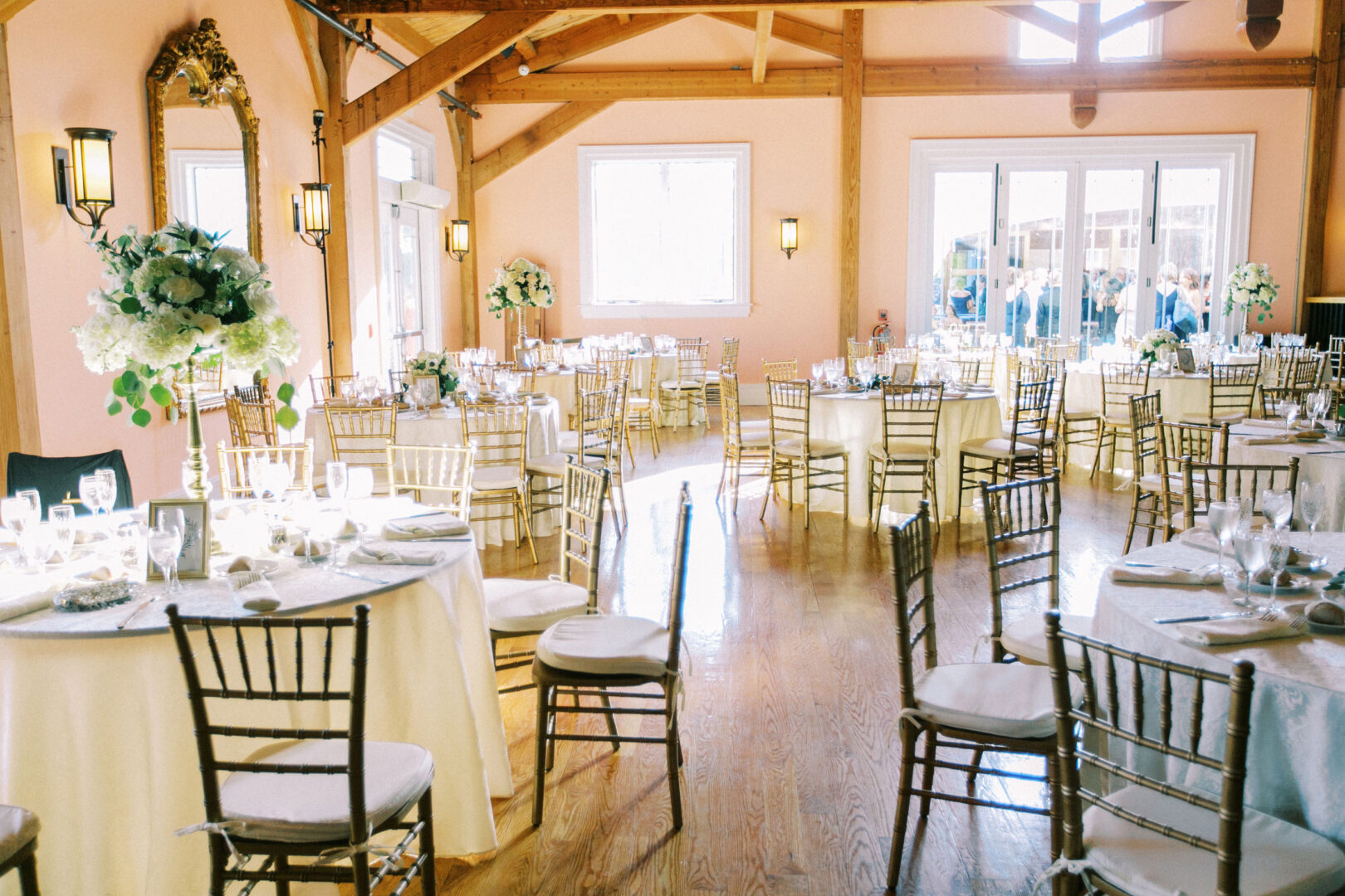 A bright banquet hall at Willow Creek Winery features round tables and gold chairs, elegantly decorated with white and green floral centerpieces.