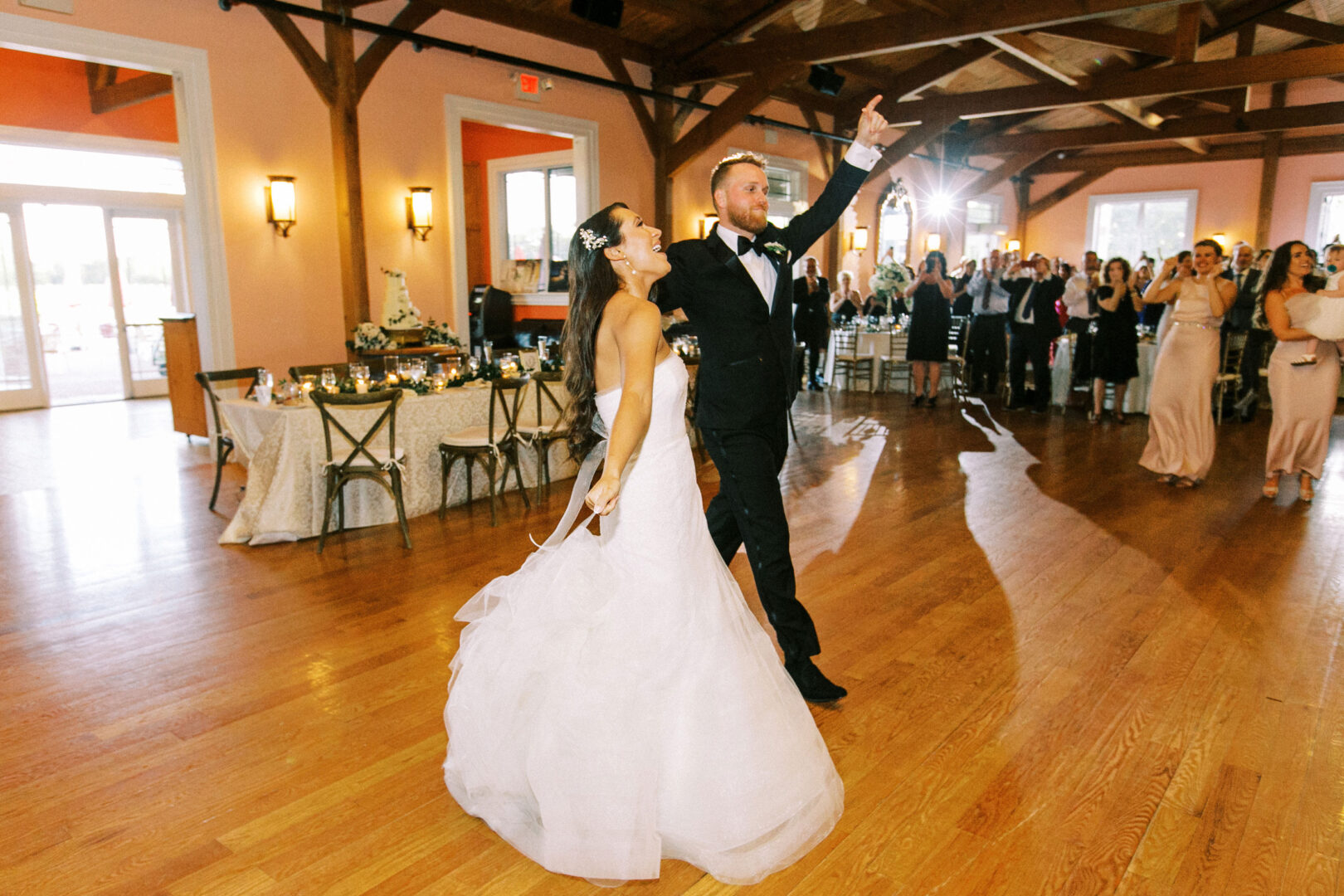 The bride and groom dance gracefully in the reception hall at Willow Creek Winery, surrounded by guests on a warm wooden floor.