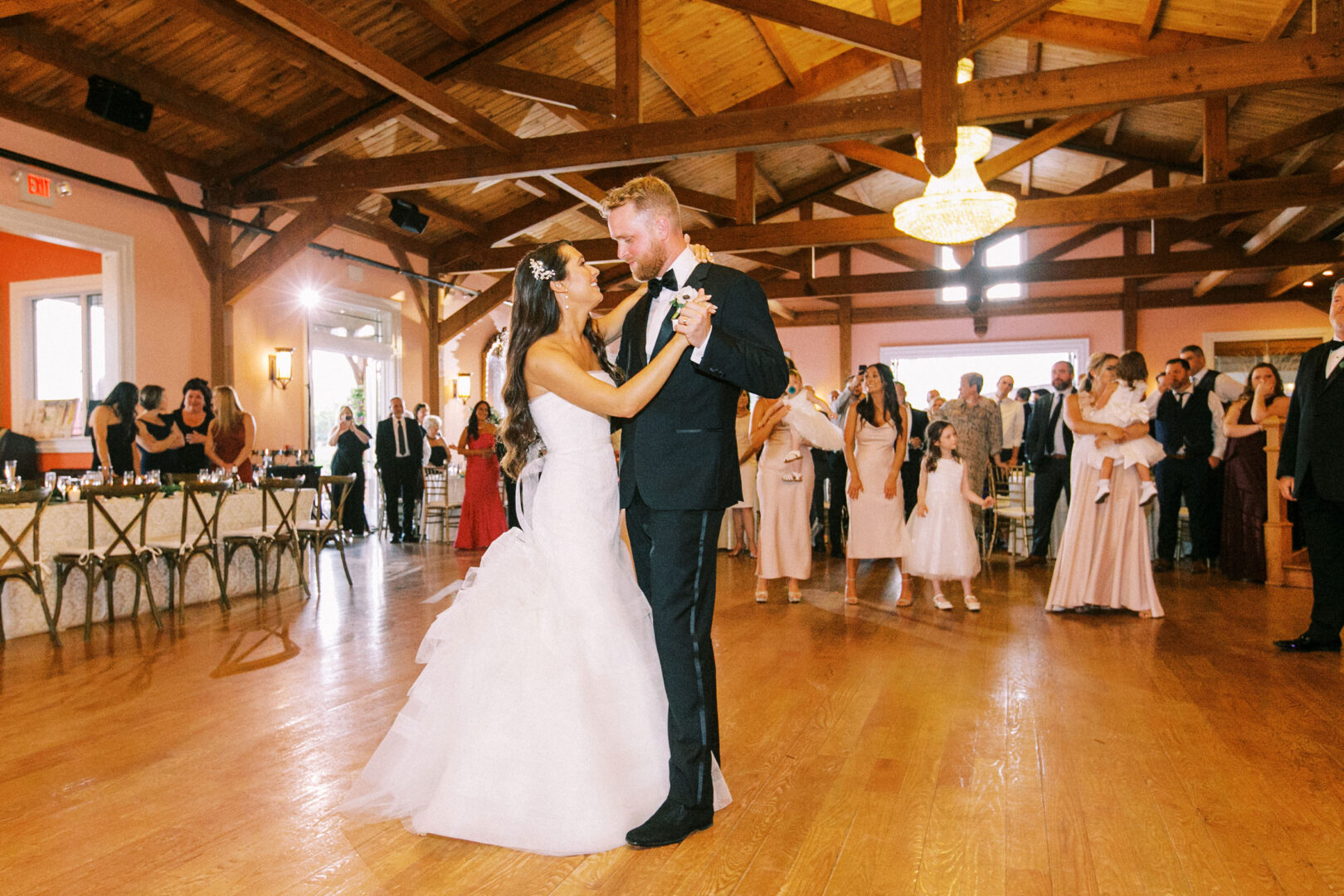 The bride and groom share their first dance at a Willow Creek Winery wedding, surrounded by guests in the warmly lit hall.