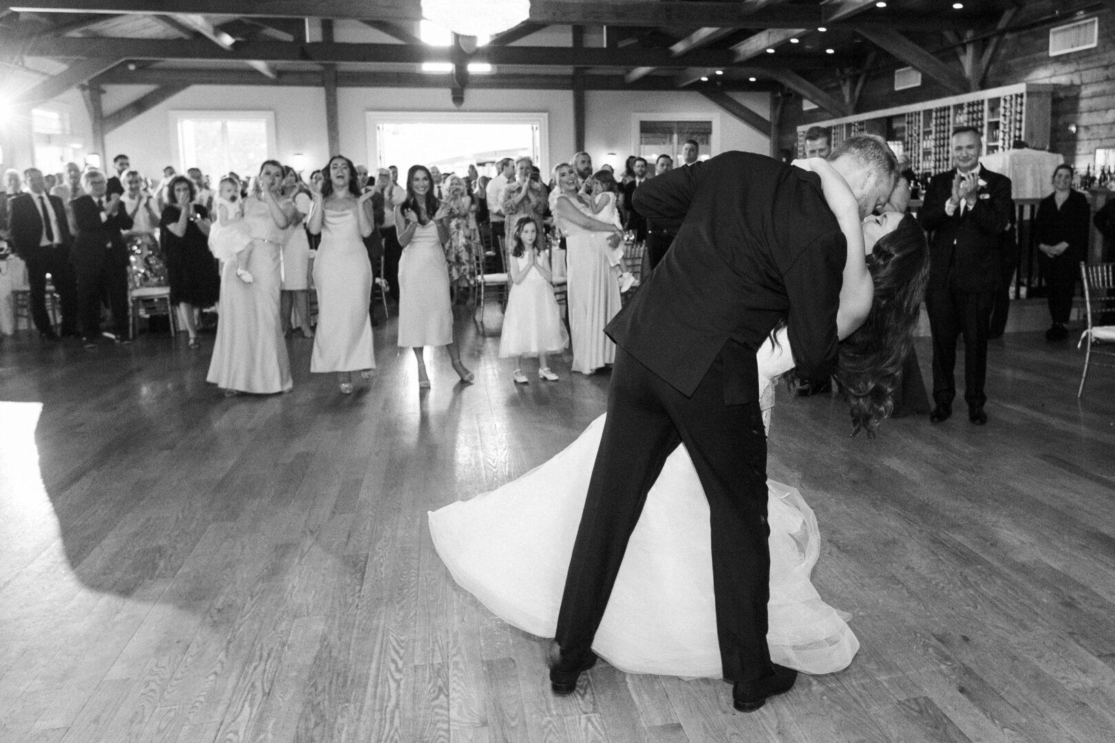 At a beautiful Willow Creek Winery wedding, a couple performs a graceful dance dip at the reception, surrounded by applauding guests dressed in elegant formal attire.