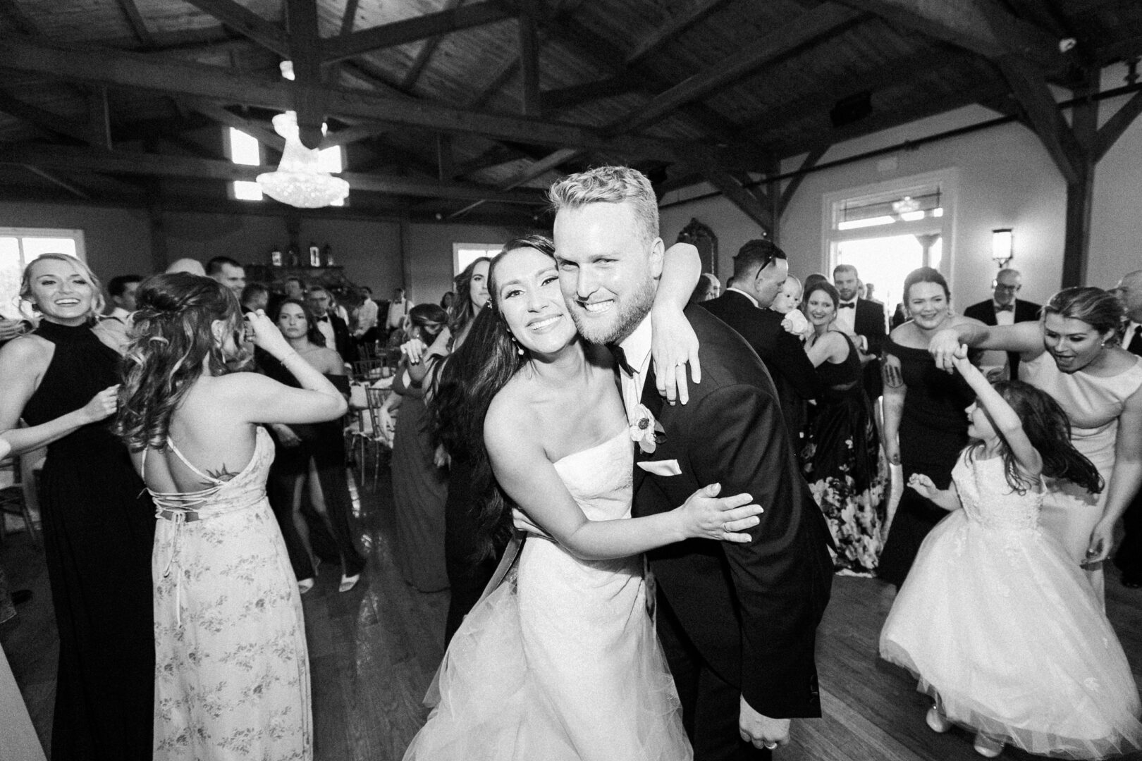 At a lively event at Willow Creek Winery, a couple embraces in the center of the dance floor, surrounded by smiling guests and a child in a dress, capturing the magic of their wedding day.