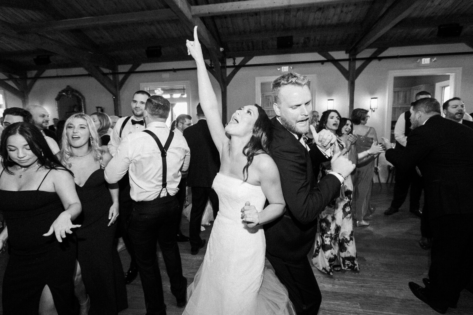 Amidst the enchanting ambiance of Willow Creek Winery, a bride and groom dance energetically in a crowded room, surrounded by joyous guests during their wedding reception.