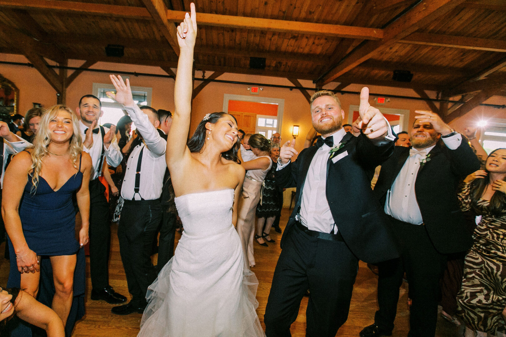 The bride and groom dance joyfully with guests on the wooden floor, celebrating their Willow Creek Winery wedding reception.