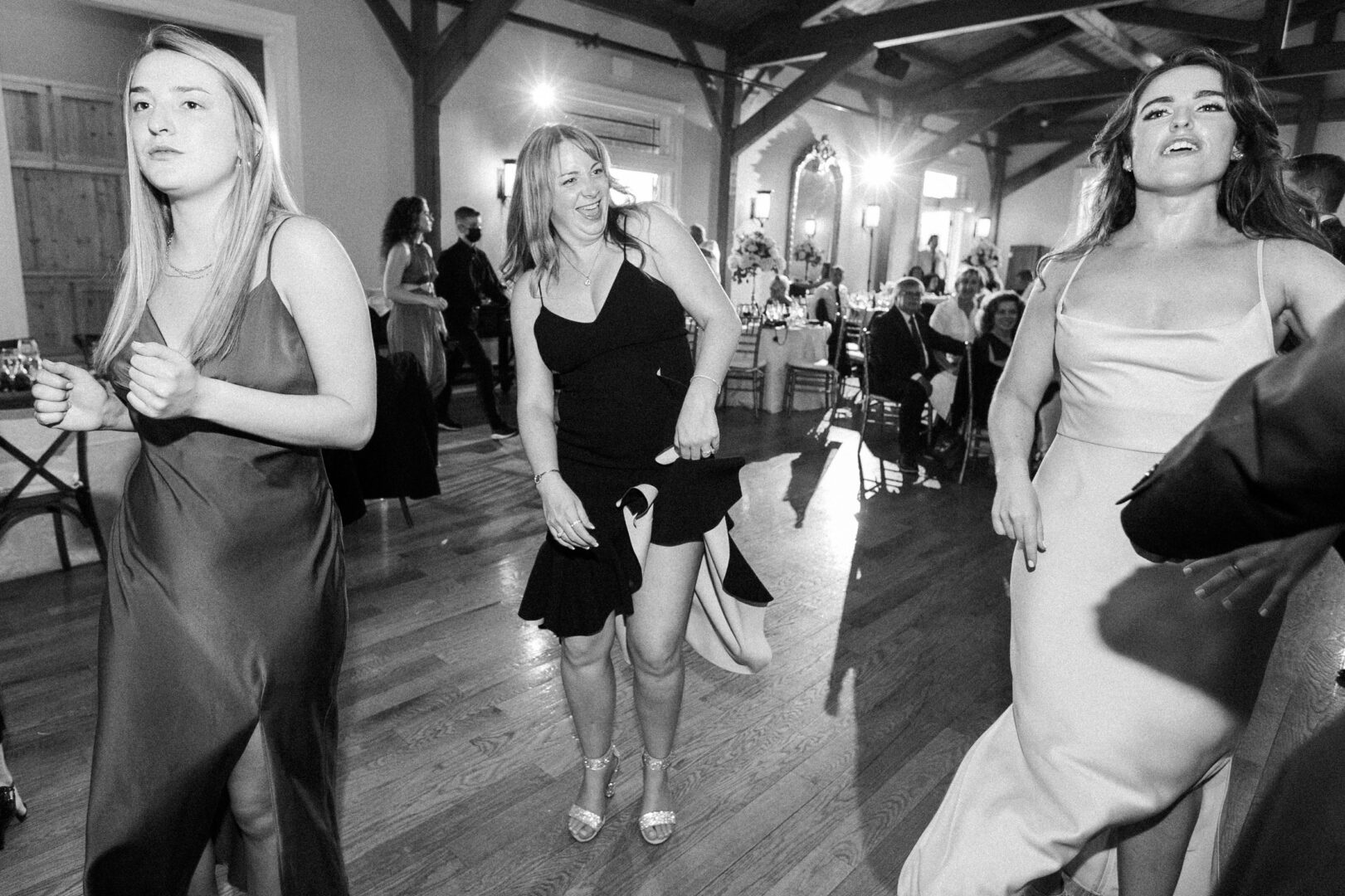 At a lively Willow Creek Winery wedding, three women in formal dresses dance gracefully, with other guests and elegant decorations visible in the background.