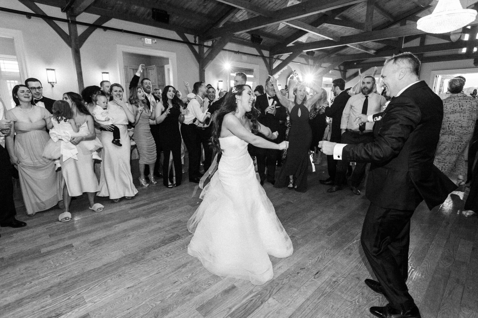 At a Willow Creek Winery wedding, the bride and groom dance joyfully on a wooden floor, surrounded by cheering guests at the reception.