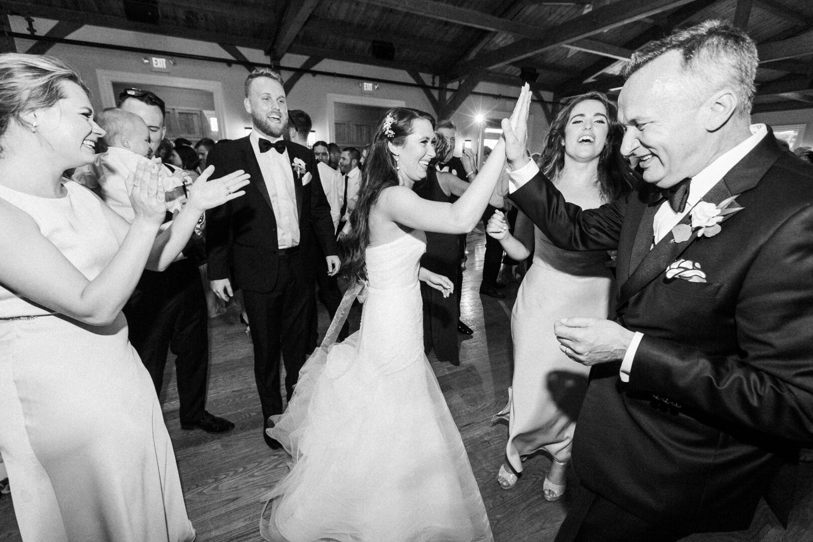 At a lively Willow Creek Winery wedding, a bride high-fives a man in a suit on the dance floor, surrounded by cheering guests.