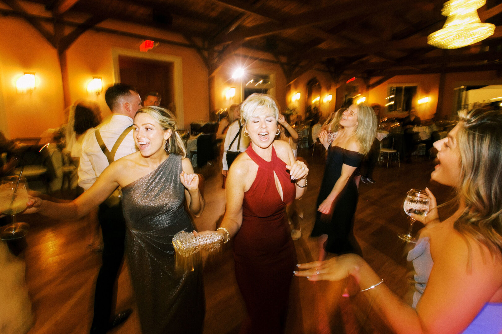 People dancing energetically at a party in a warmly lit room, holding drinks and smiling, reminiscent of a joyous celebration at Willow Creek Winery Wedding.