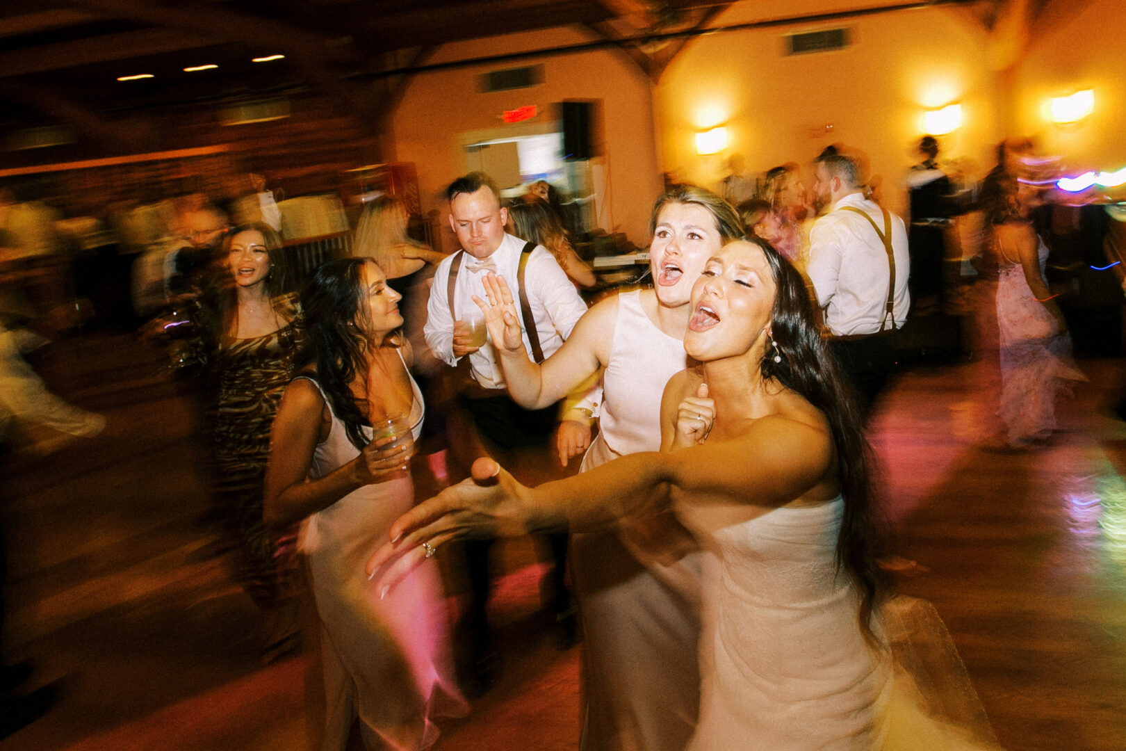 A joyful group of people dancing energetically at an indoor Willow Creek Winery wedding, with dim lighting and blurred motion capturing their excitement.