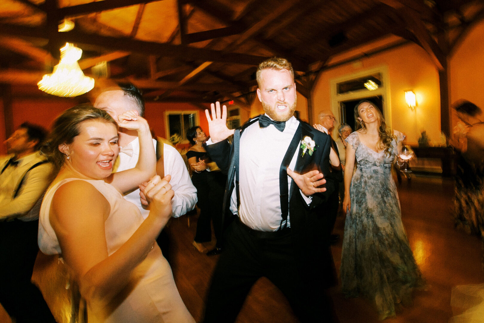 At the lively Willow Creek Winery wedding, a man in a tuxedo enthusiastically dances alongside two women, bringing an extra spark to the indoor celebration.