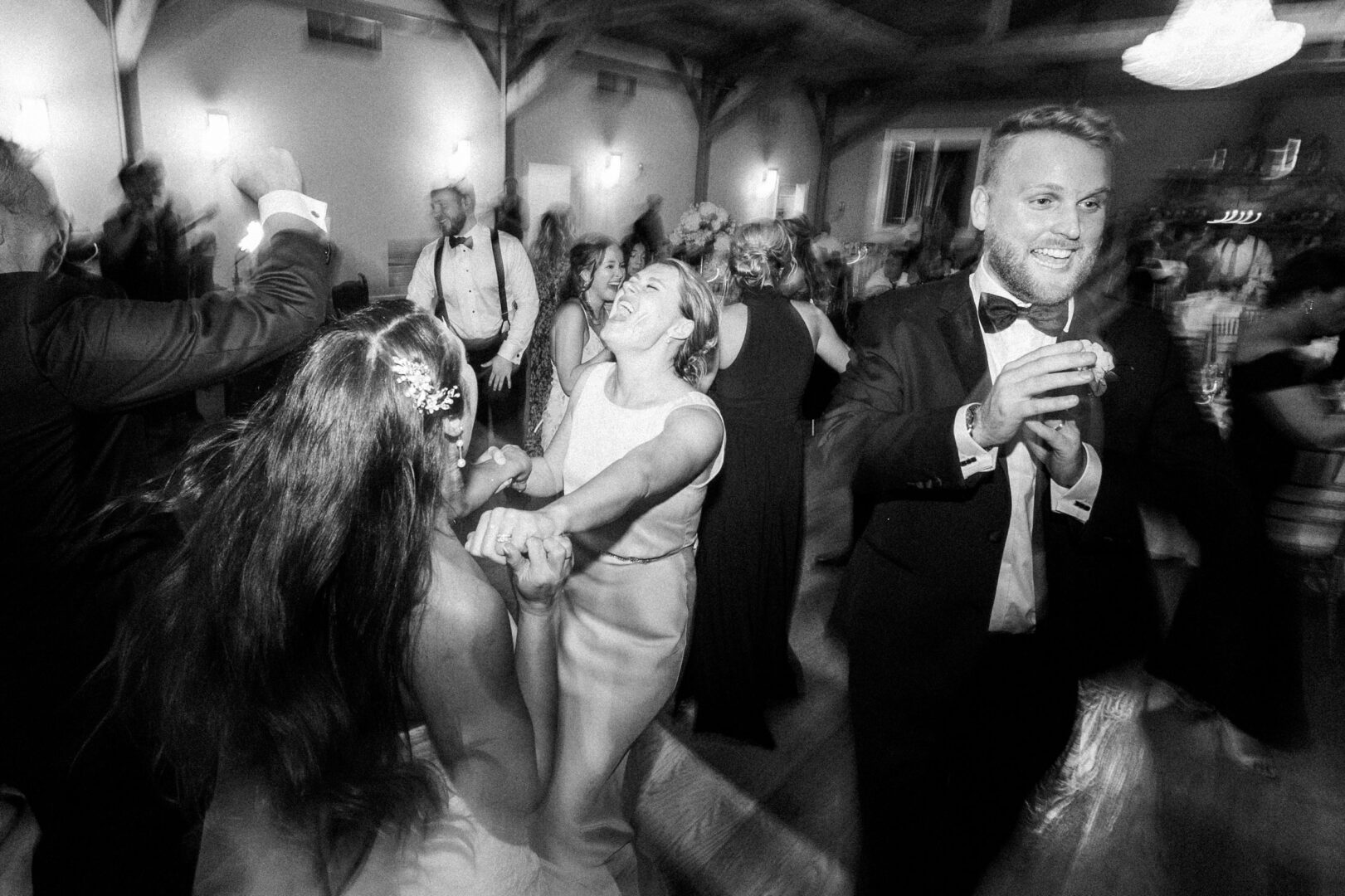 Black and white photo of people dancing at a lively Willow Creek Winery wedding. Individuals are dressed in formal attire, with joyful expressions, moving energetically on the dance floor.