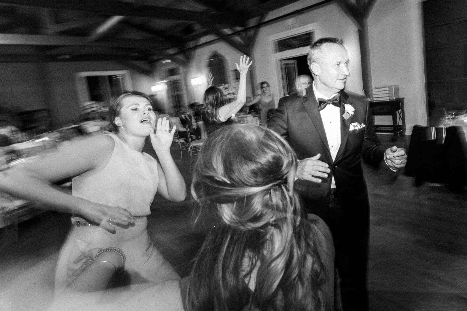 At the Willow Creek Winery Wedding, people were dancing energetically at the indoor event; a black and white photo capturing movement and joy.