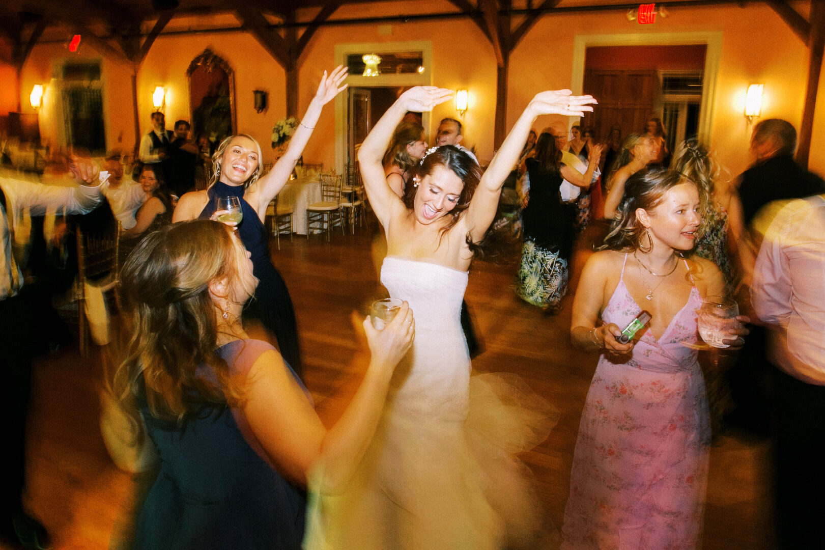 People dancing enthusiastically at a lively indoor event, with colorful lighting and drinks in hand, reminiscent of the vibrant celebrations often seen at Willow Creek Winery weddings.