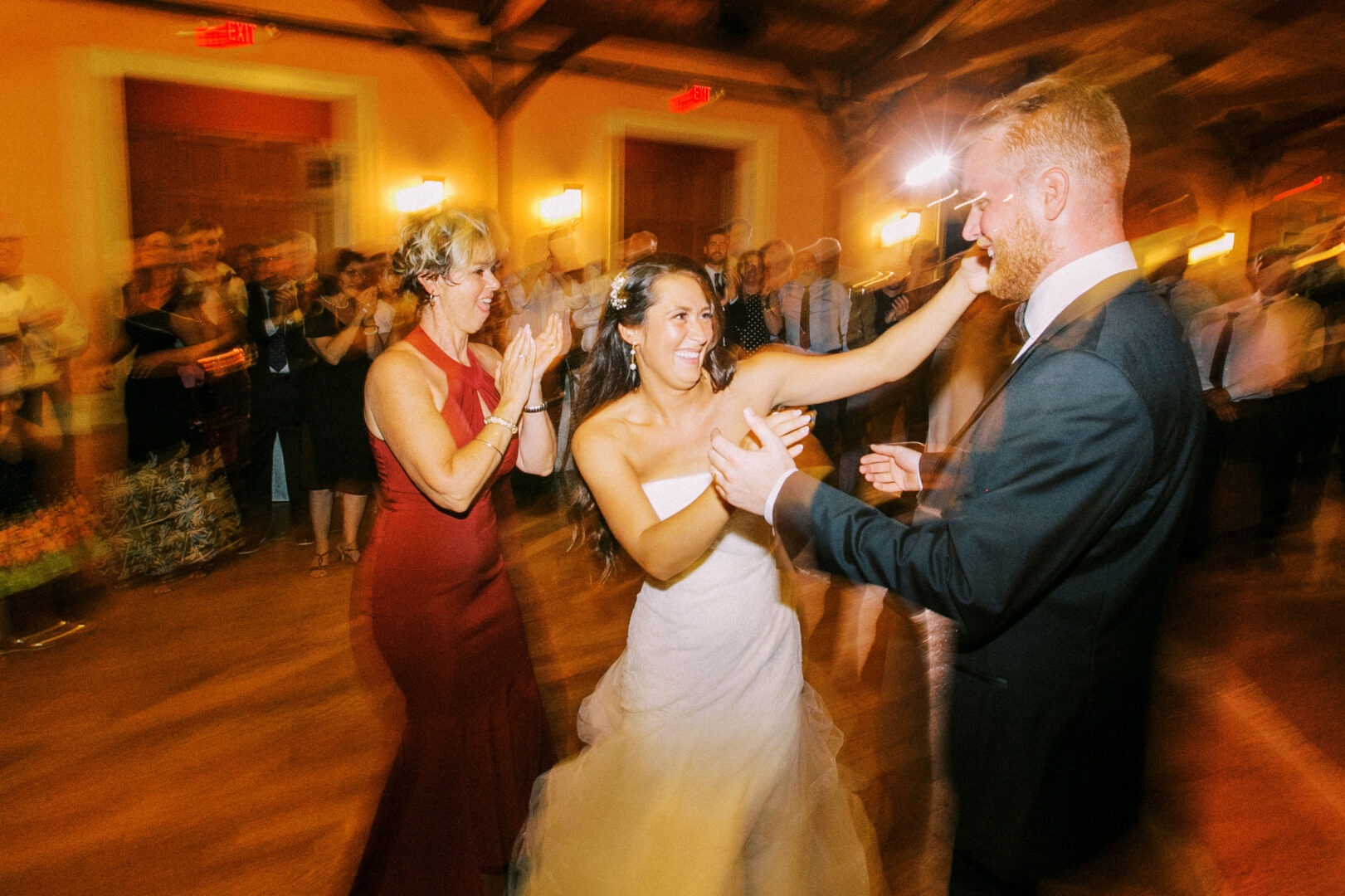 At their Willow Creek Winery wedding, the bride and groom dance joyfully at the reception, surrounded by applauding guests in a warmly lit room.