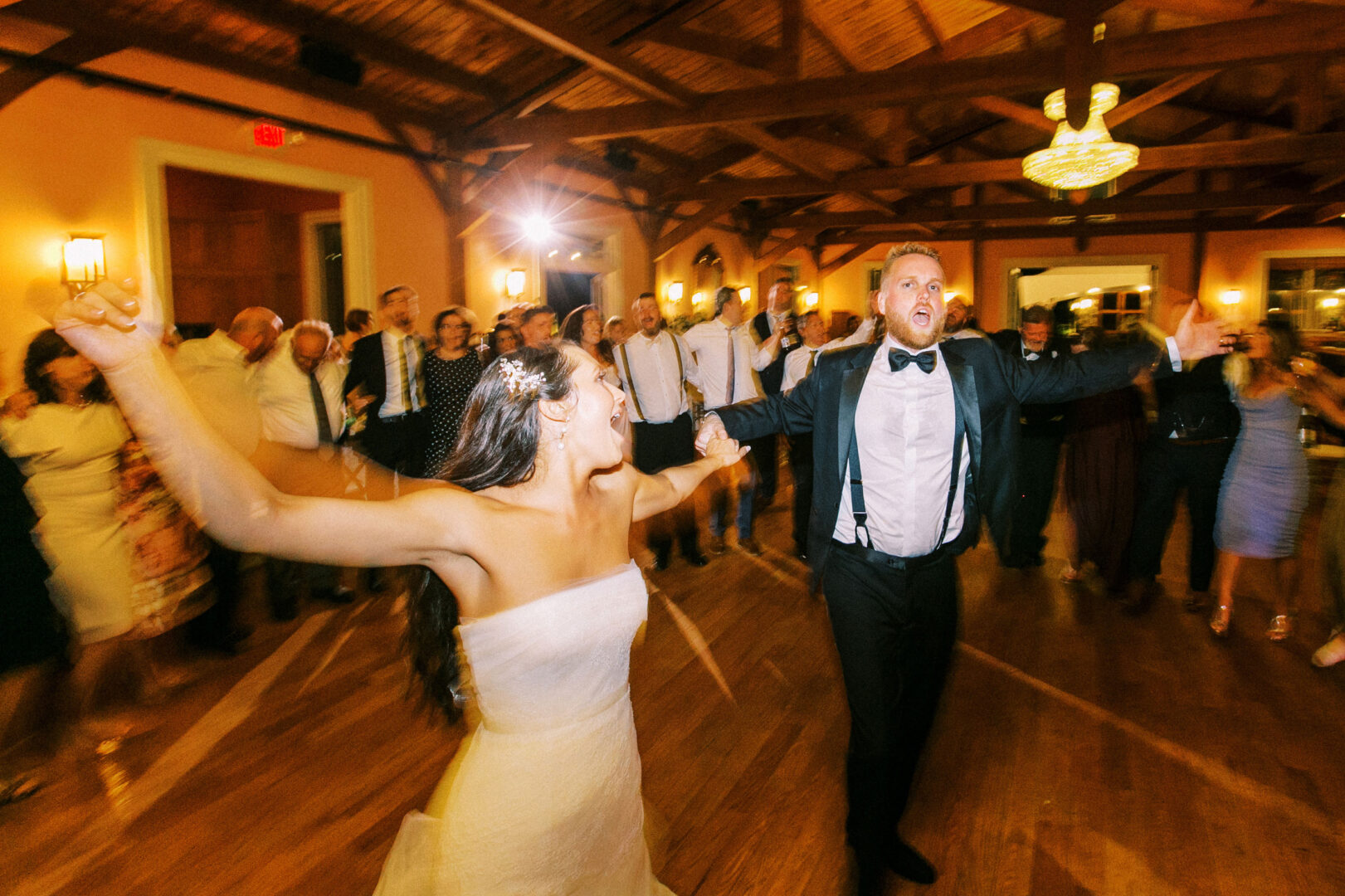 At a Willow Creek Winery wedding, a bride and groom dance energetically in a lively, crowded room with wooden beams and glowing lights.