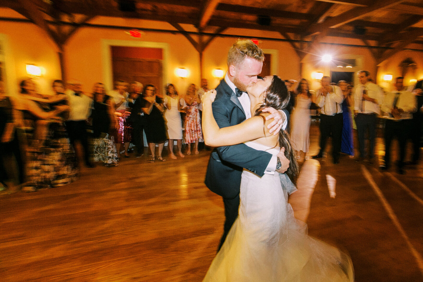 Amid the lively atmosphere of their Willow Creek Winery wedding, a couple shares a tender kiss while dancing in a large room filled with an appreciative crowd gathered around them.