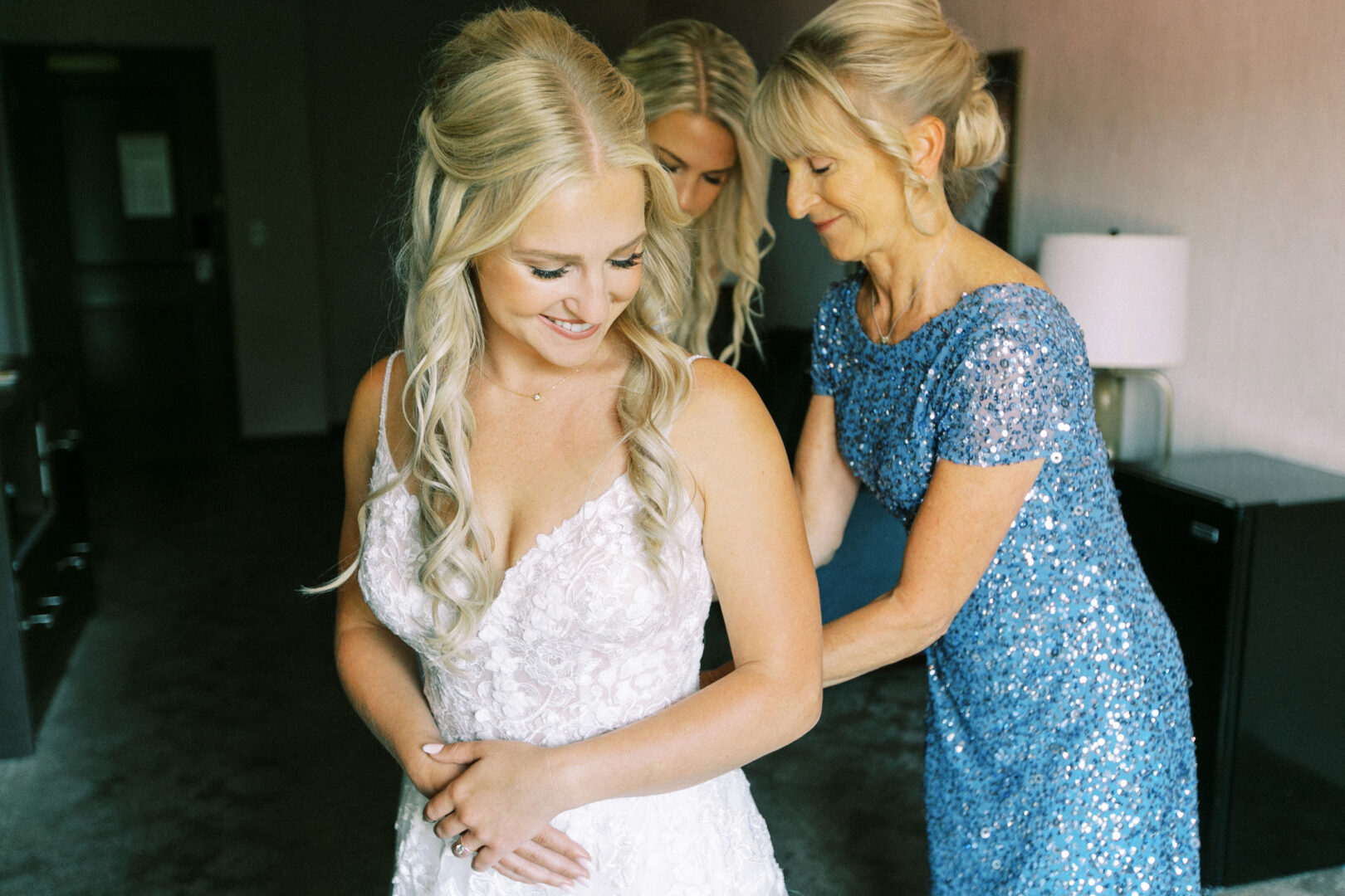 At the charming Normandy Farm Wedding, the bride beams with joy as two women assist her with her elegant wedding dress.