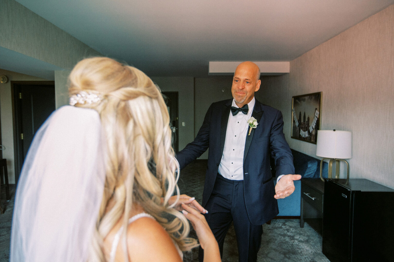 A man in a suit and a woman in a bridal gown with a veil stand facing each other in the elegant ambiance of Normandy Farm, capturing the essence of their wedding day.