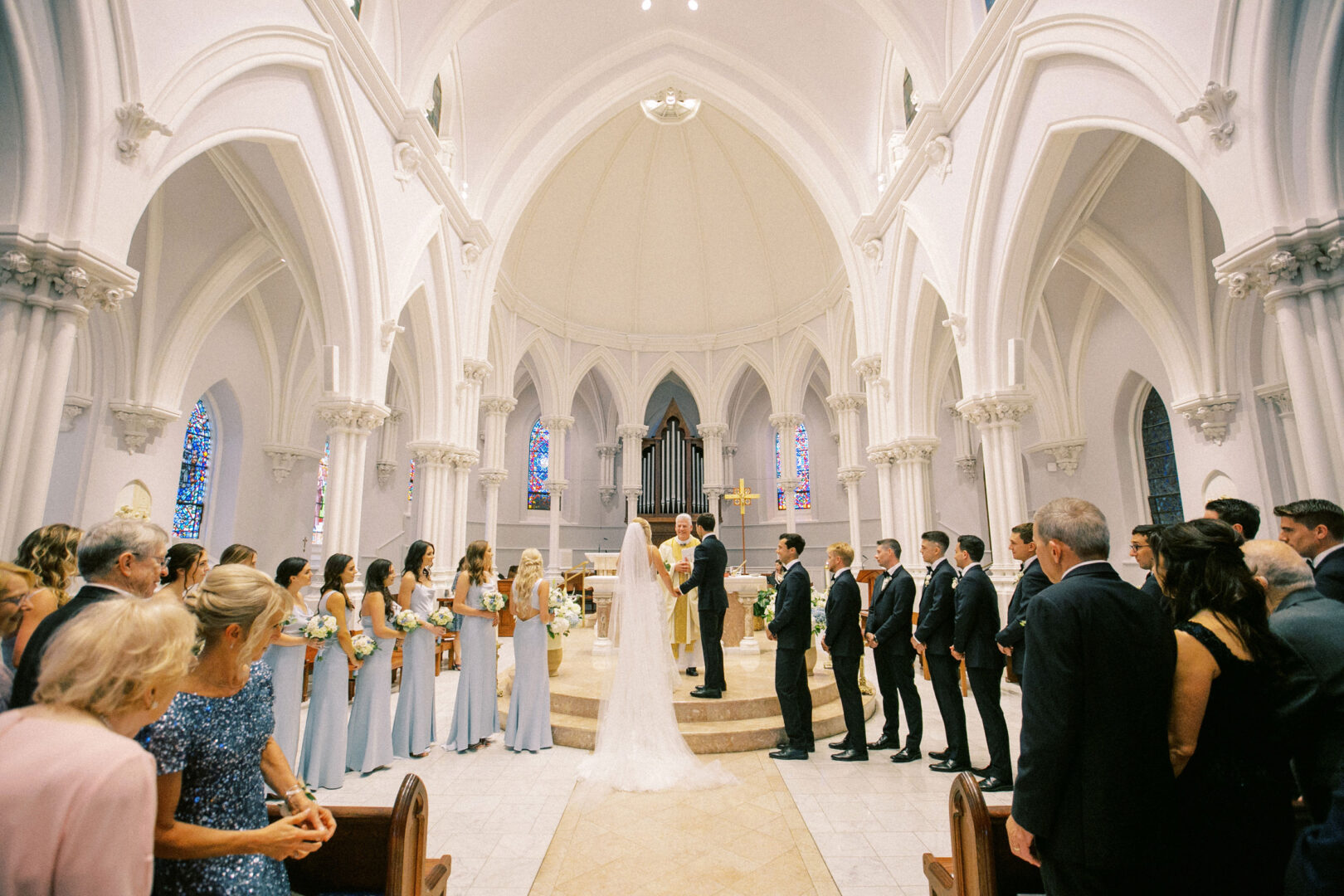 A Normandy Farm wedding graced by a bride and groom at the church altar, surrounded by their bridal party, with guests seated in pews celebrating this beautiful union.