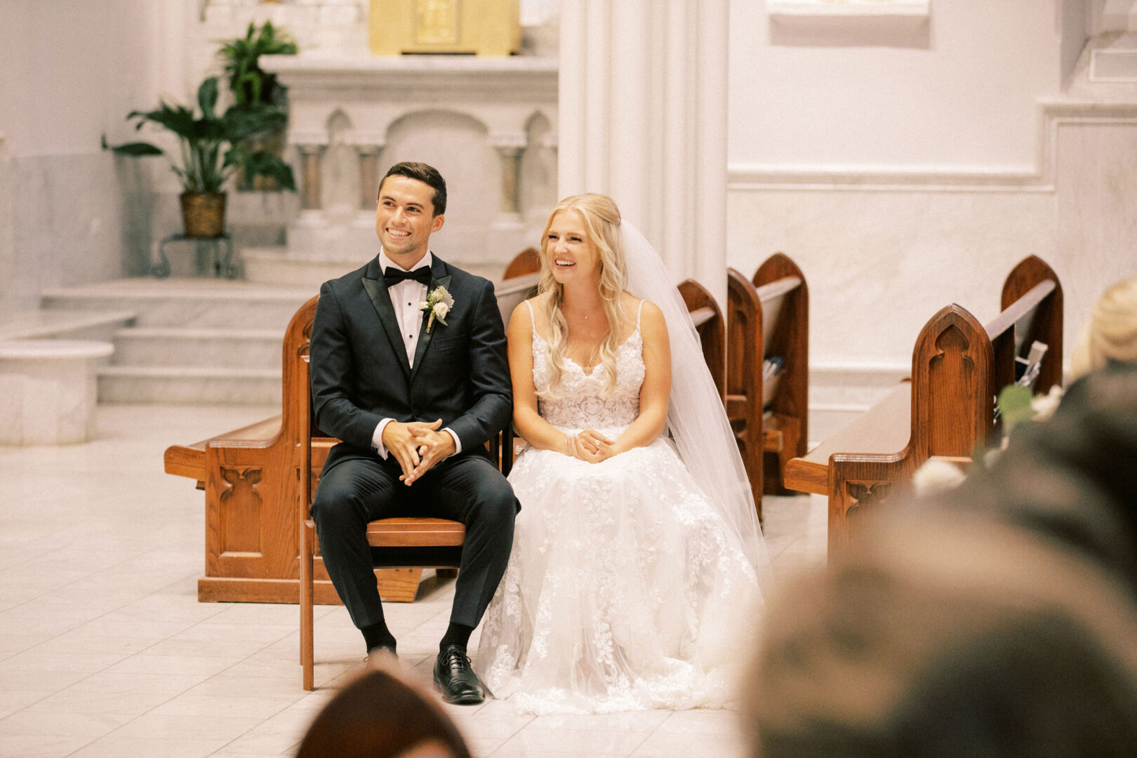 A bride and groom sit inside a church, smiling brightly in their formal wedding attire, the spirit of a Normandy Farm Wedding echoing through their joy-filled eyes.