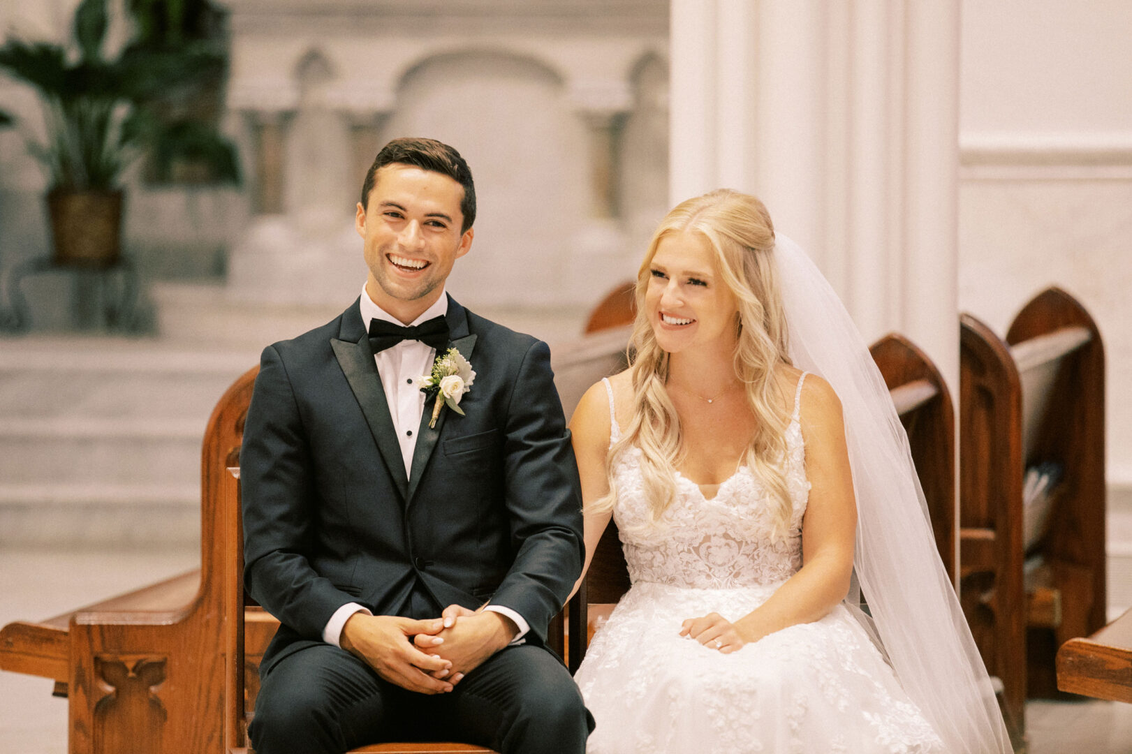 A bride and groom sit on chairs in a church setting, dressed in formal wedding attire, capturing the elegance of a Normandy Farm Wedding.