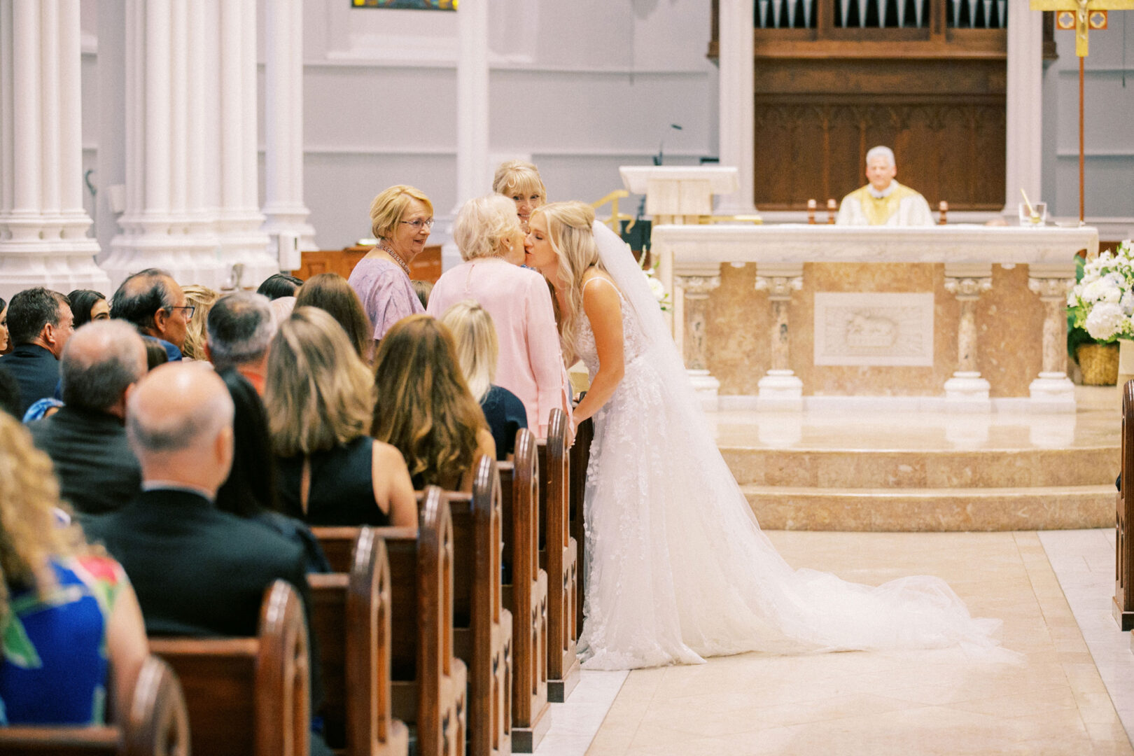 At a Normandy Farm wedding, a bride in a white dress leans forward to greet guests seated in church pews during the ceremony.