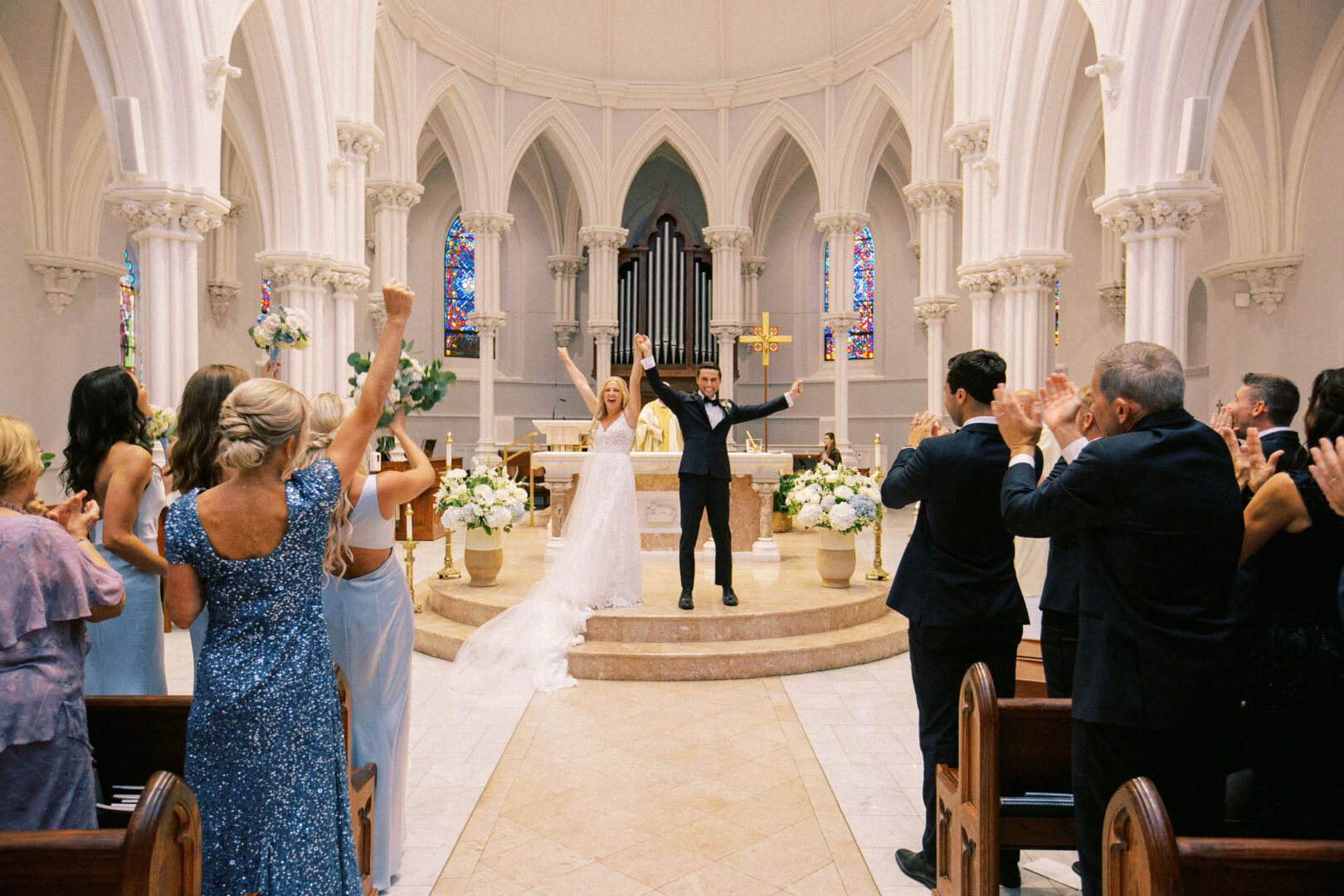 A bride and groom celebrate on the altar of a church amidst the rustic charm of a Normandy Farm wedding, surrounded by cheering guests.