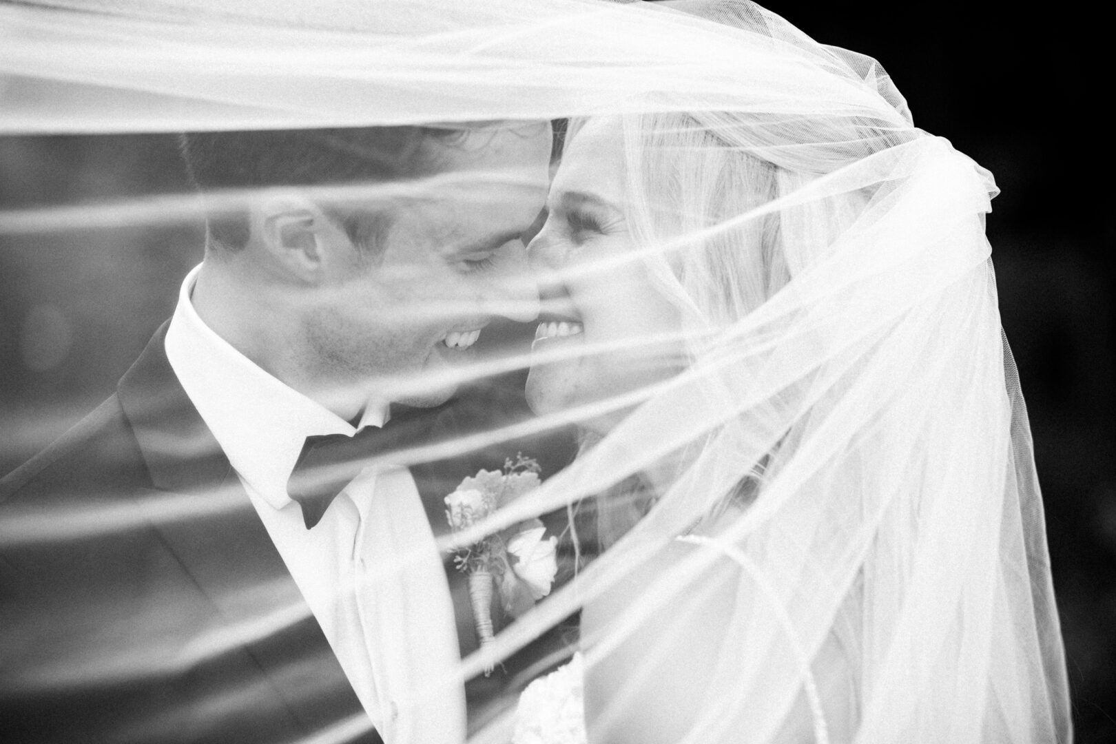 A bride and groom smiling under a flowing veil on their Normandy Farm wedding day.