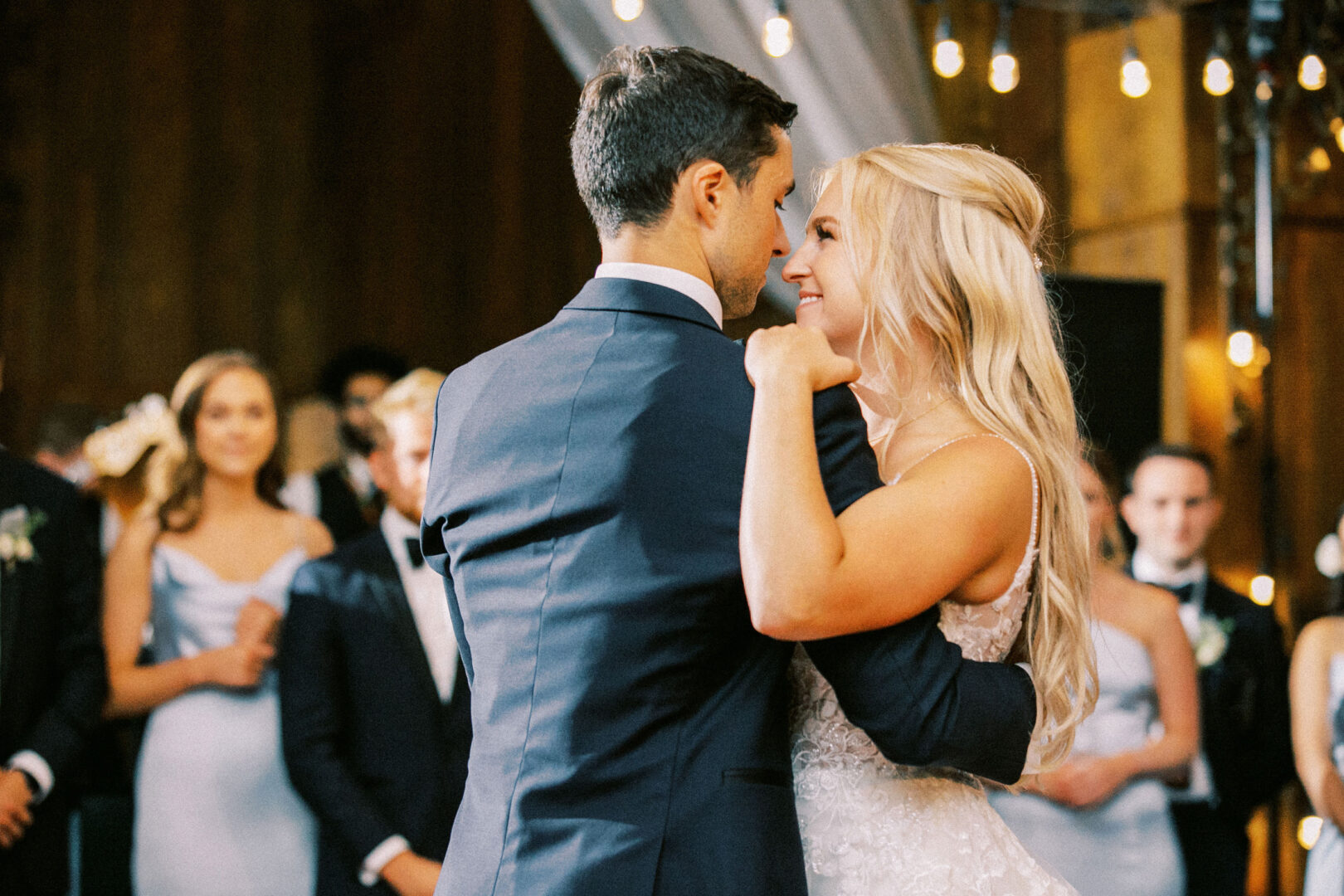 Amidst the charm of a Normandy Farm wedding, a bride and groom share a dance at their reception, surrounded by delighted guests.