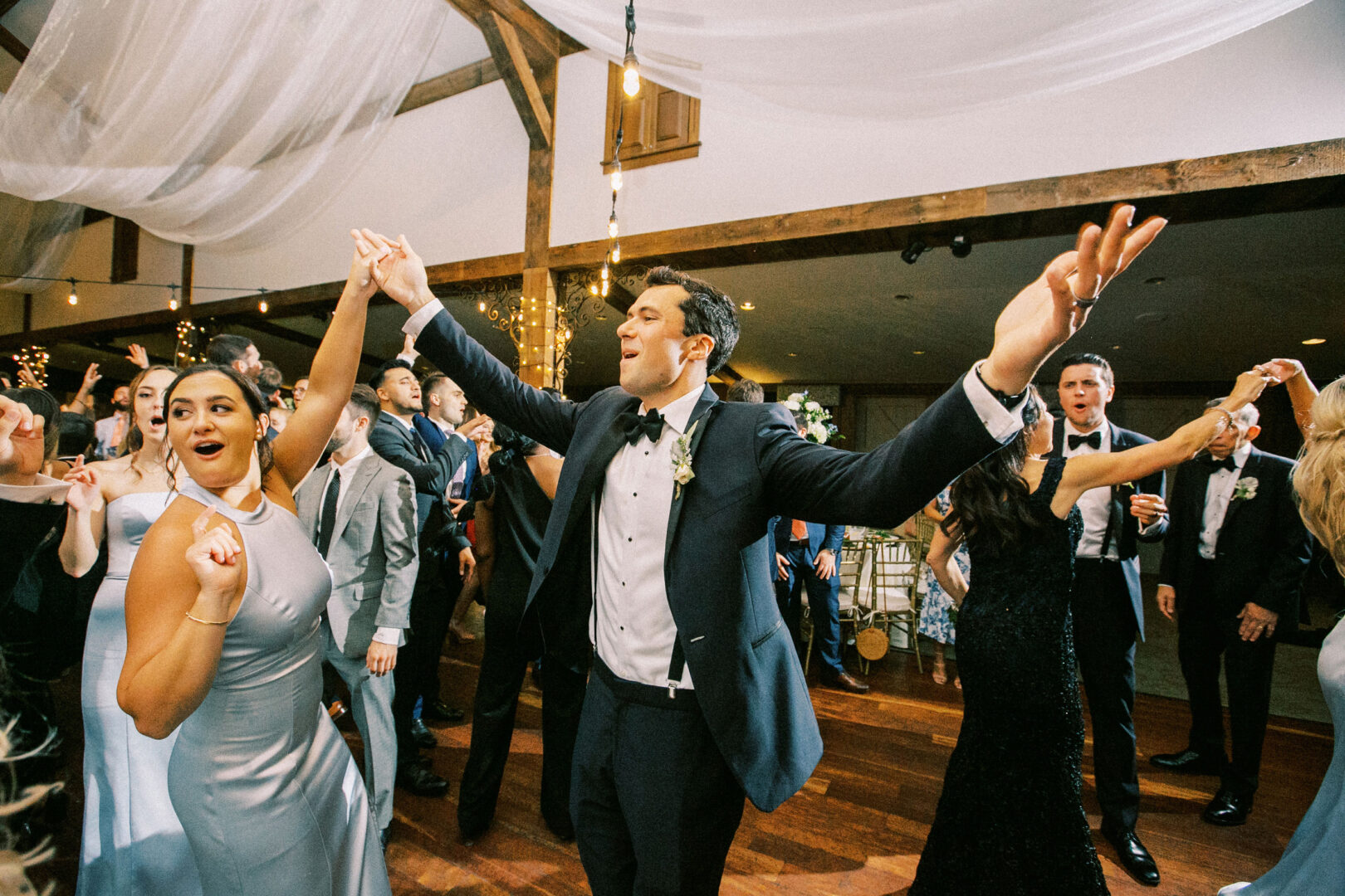 Amid the lively crowd at a Normandy Farm wedding, a man in a tuxedo dances enthusiastically, capturing the joyful spirit of the formal event.