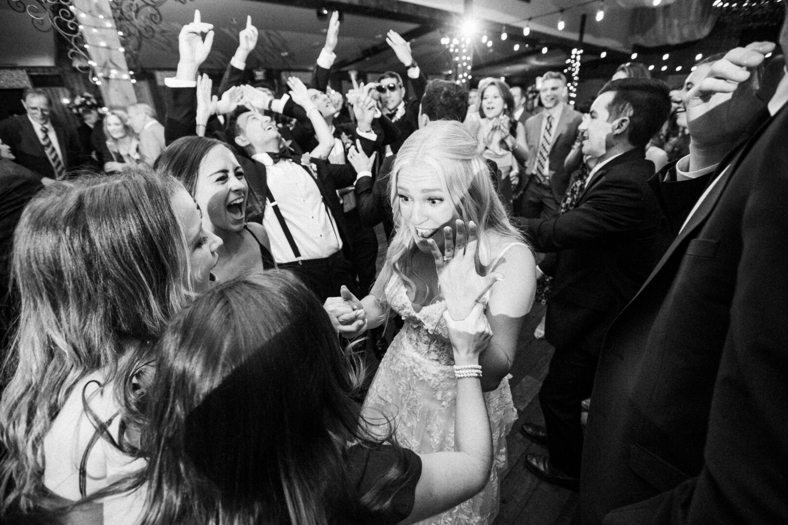 At a lively Normandy Farm Wedding, a woman in a formal dress covers her mouth in surprise while laughing, surrounded by cheering guests.