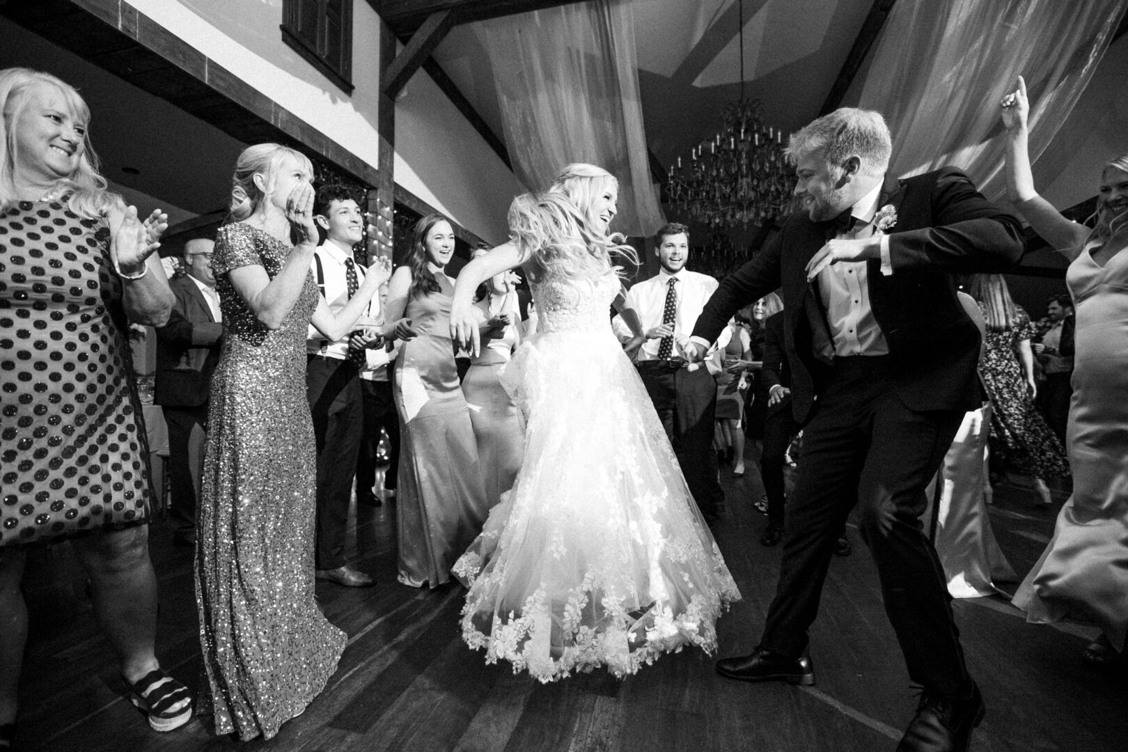 At a lively Normandy Farm wedding, the bride and groom dance energetically on the floor, surrounded by cheering guests. The scene is pure celebration.